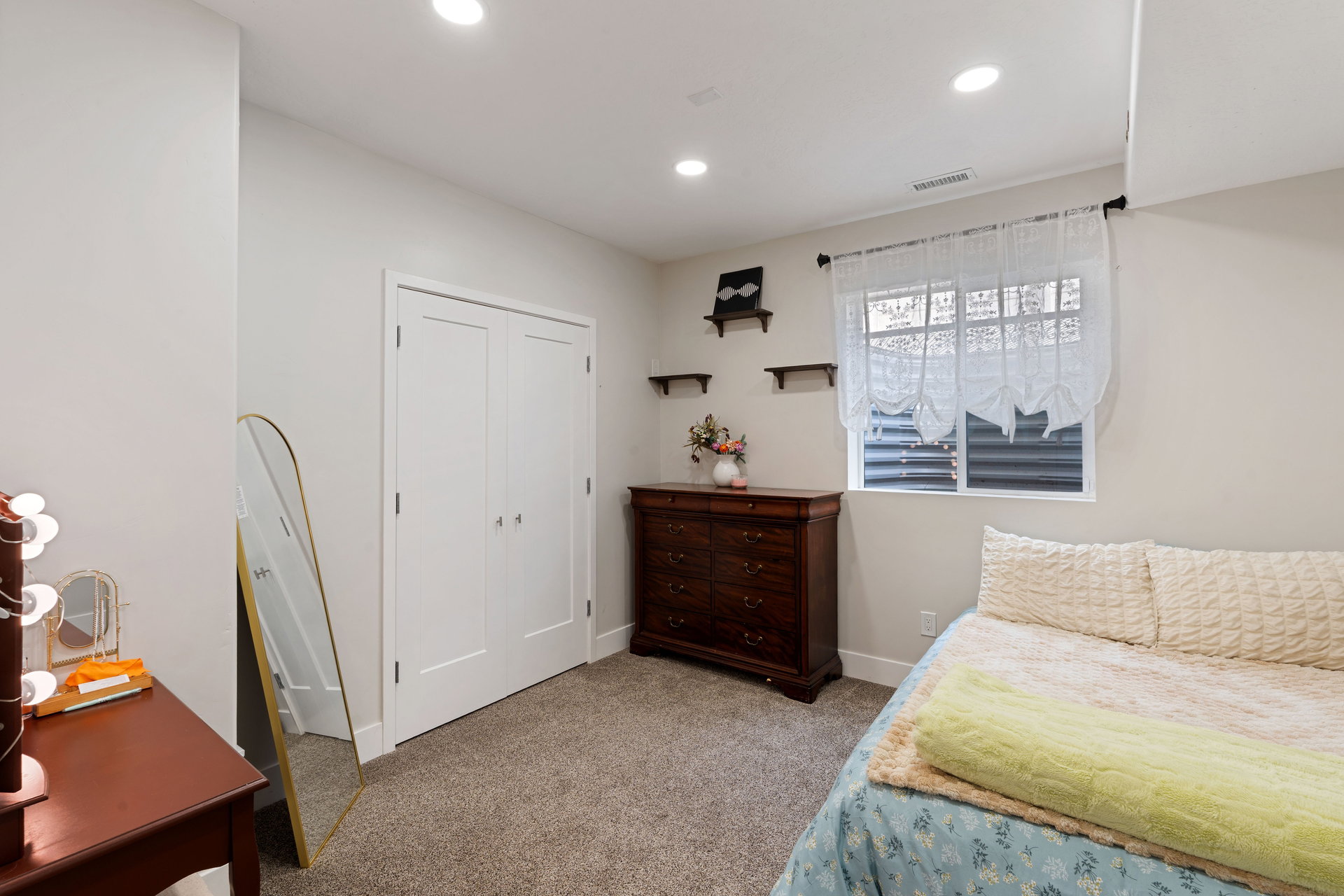 Basement bedroom with recessed lighting illuminates a carpeted room featuring a double-door closet with contemporary hardware