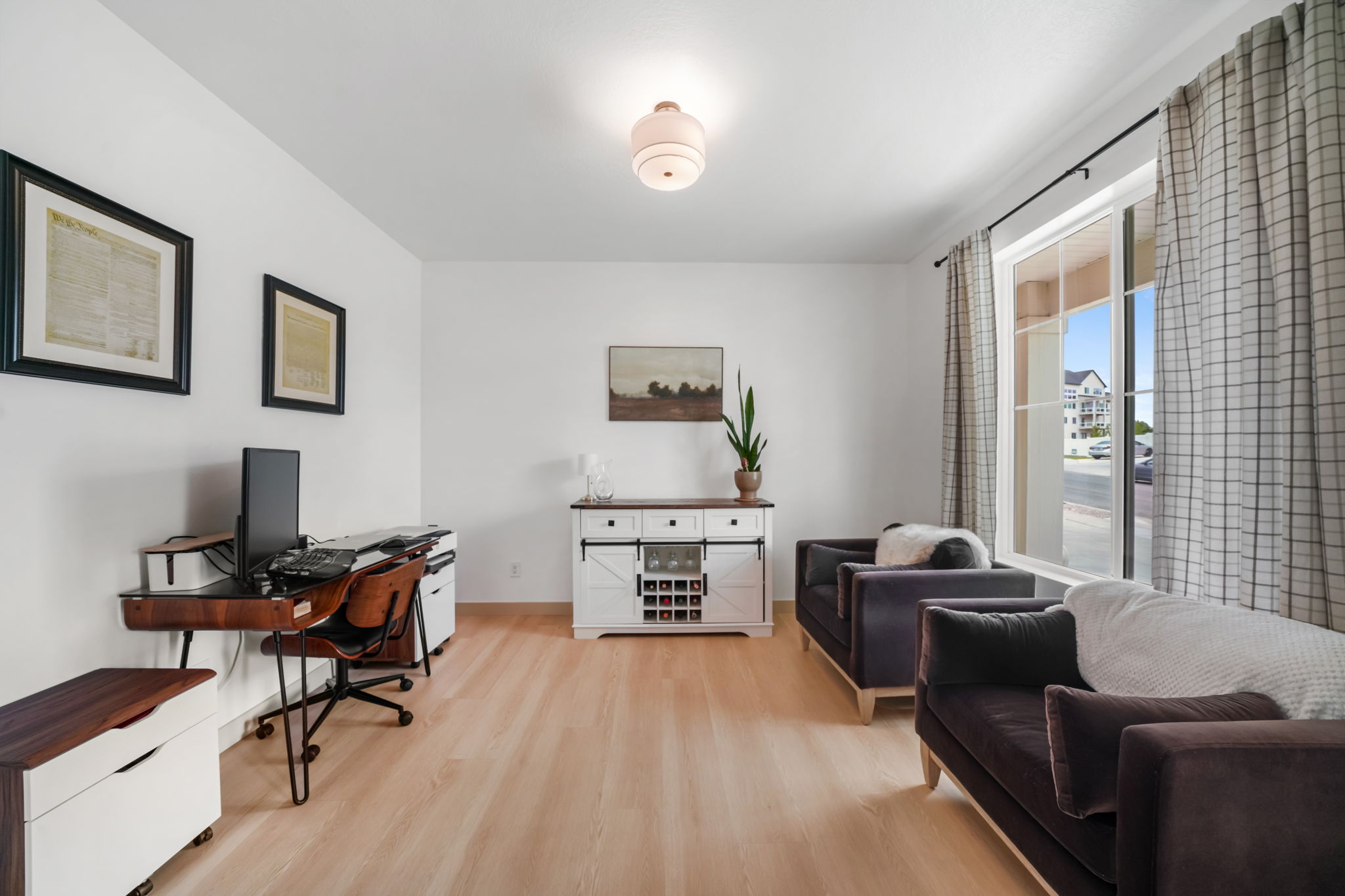 Bright room featuring wood-finish flooring, white walls, and a large window with checker-patterned draperies