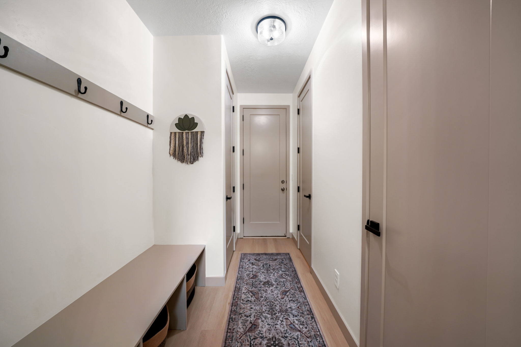 Entryway featuring light wood-finish flooring, a built-in bench with storage, a wall-mounted coat rack, and recessed panel doors with matte black hardware