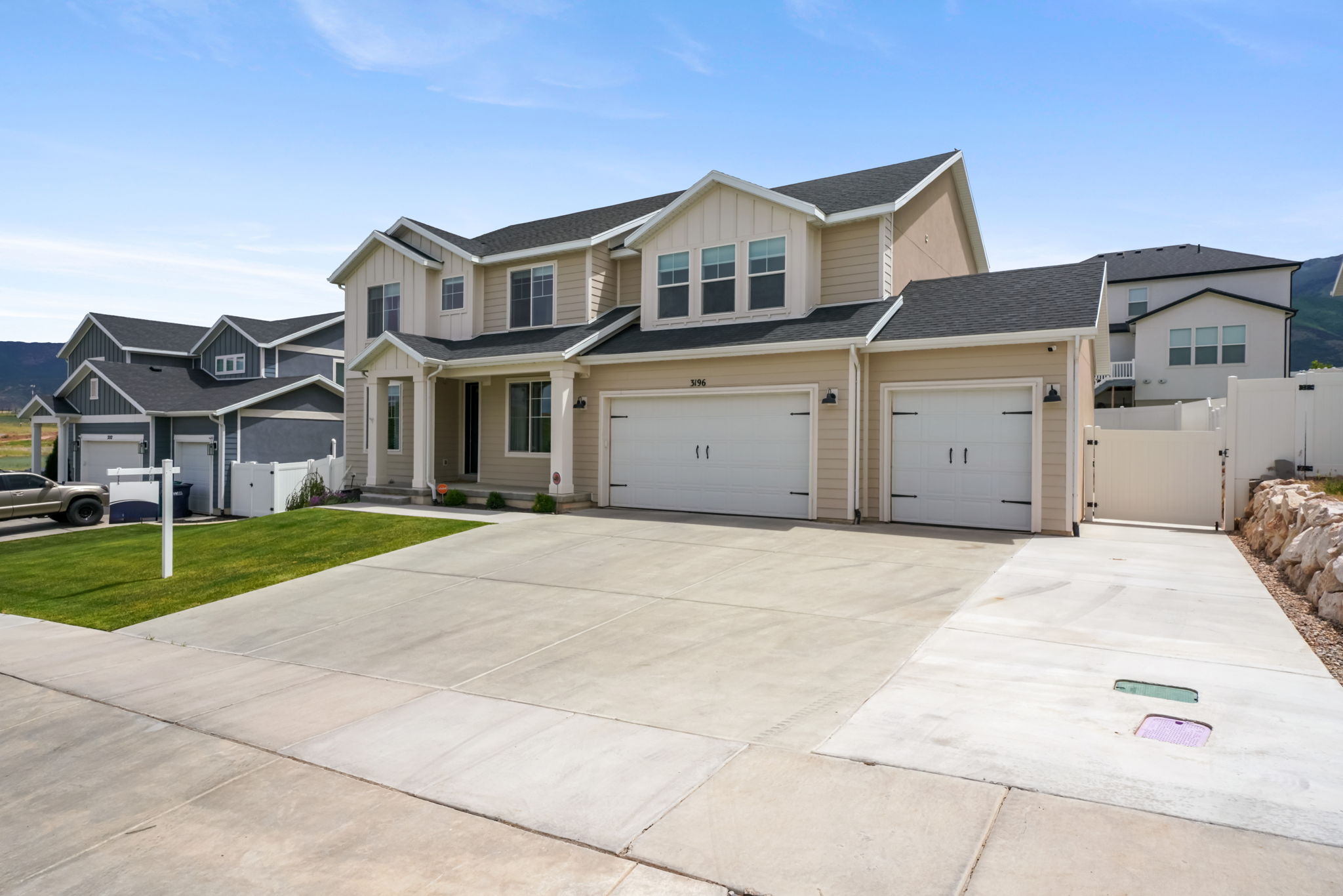 Contemporary two-story residence featuring light beige siding with white trim, dark shingle roofing, an attached three-car garage, and a concrete driveway