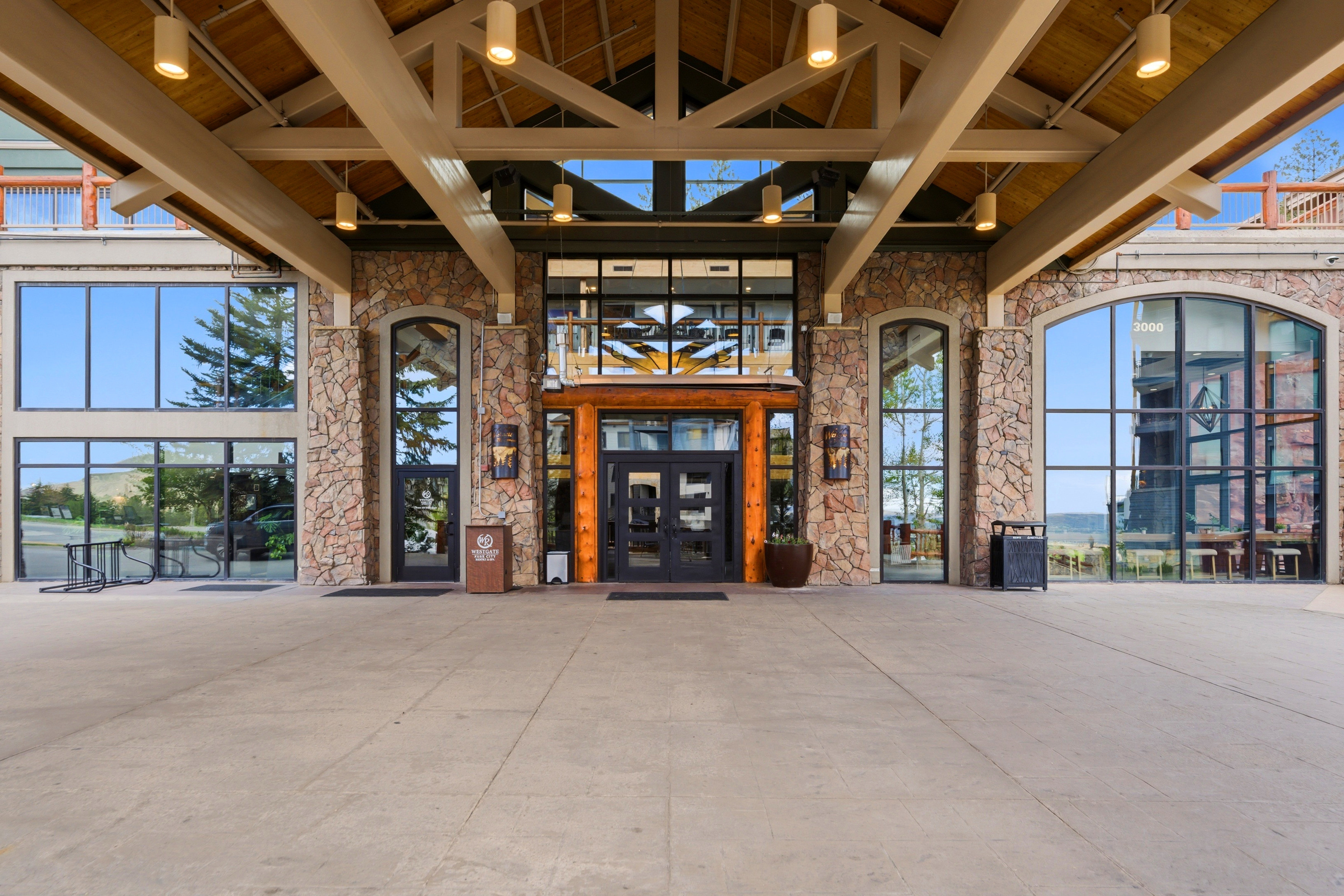 Grand entry featuring a stone and timber facade, expansive glass panels, exposed beam ceiling, and overhead lighting