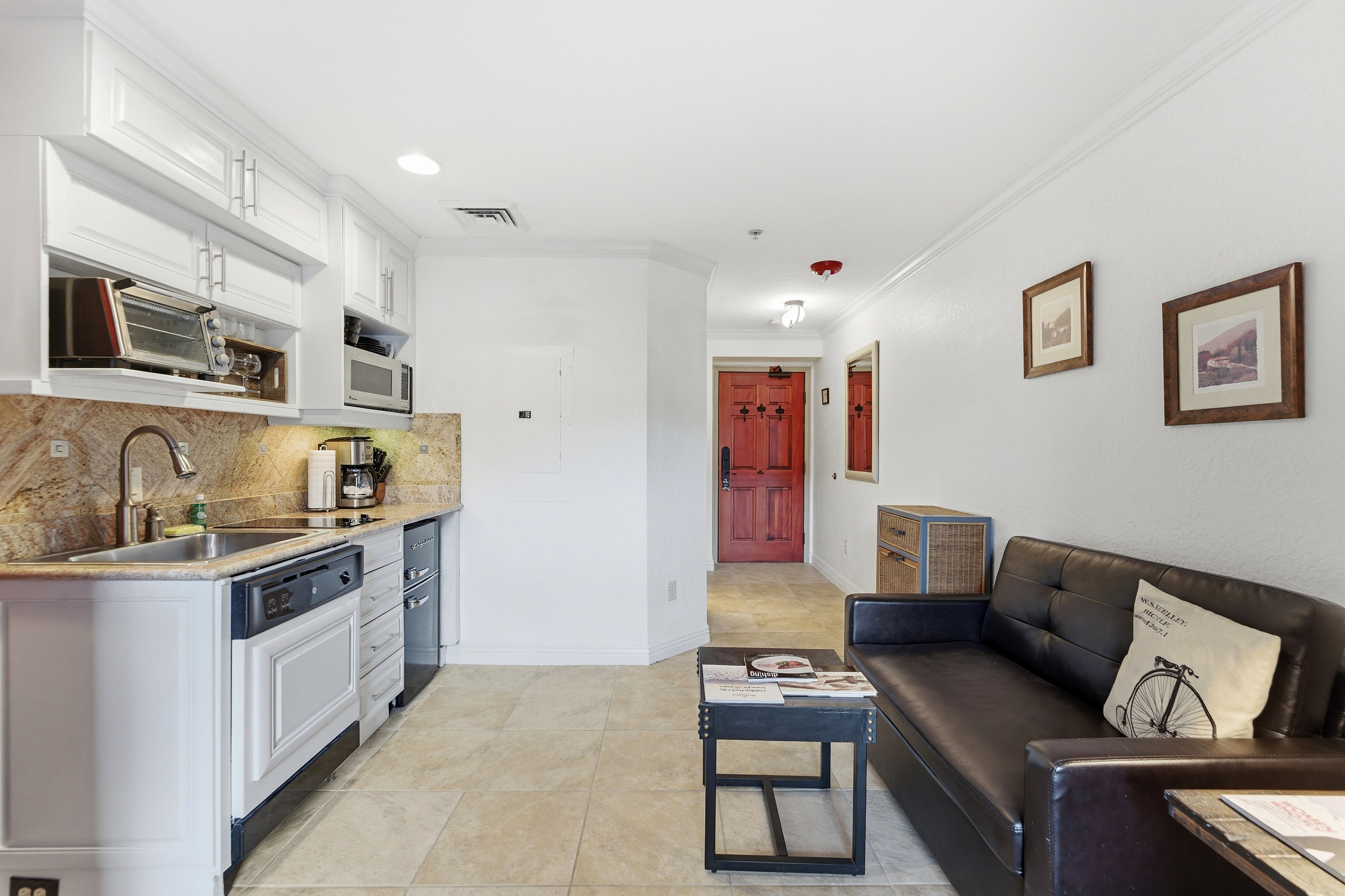 Open-concept living space featuring a modern kitchenette, tile flooring, and a distinct red entry door