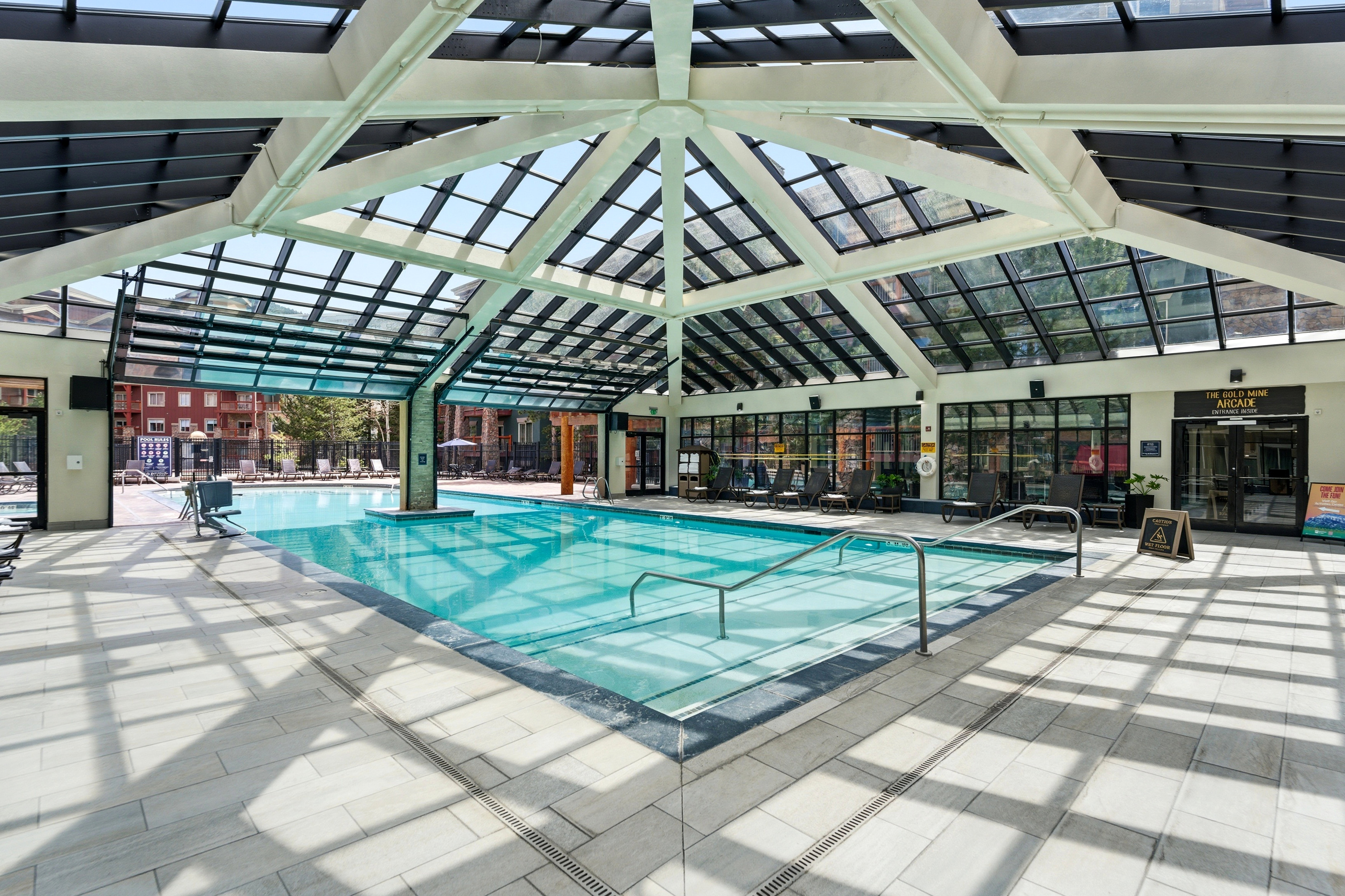 Indoor-outdoor aquatic facility featuring a large swimming pool, expansive glass ceiling, perimeter windows, and light-toned tile flooring