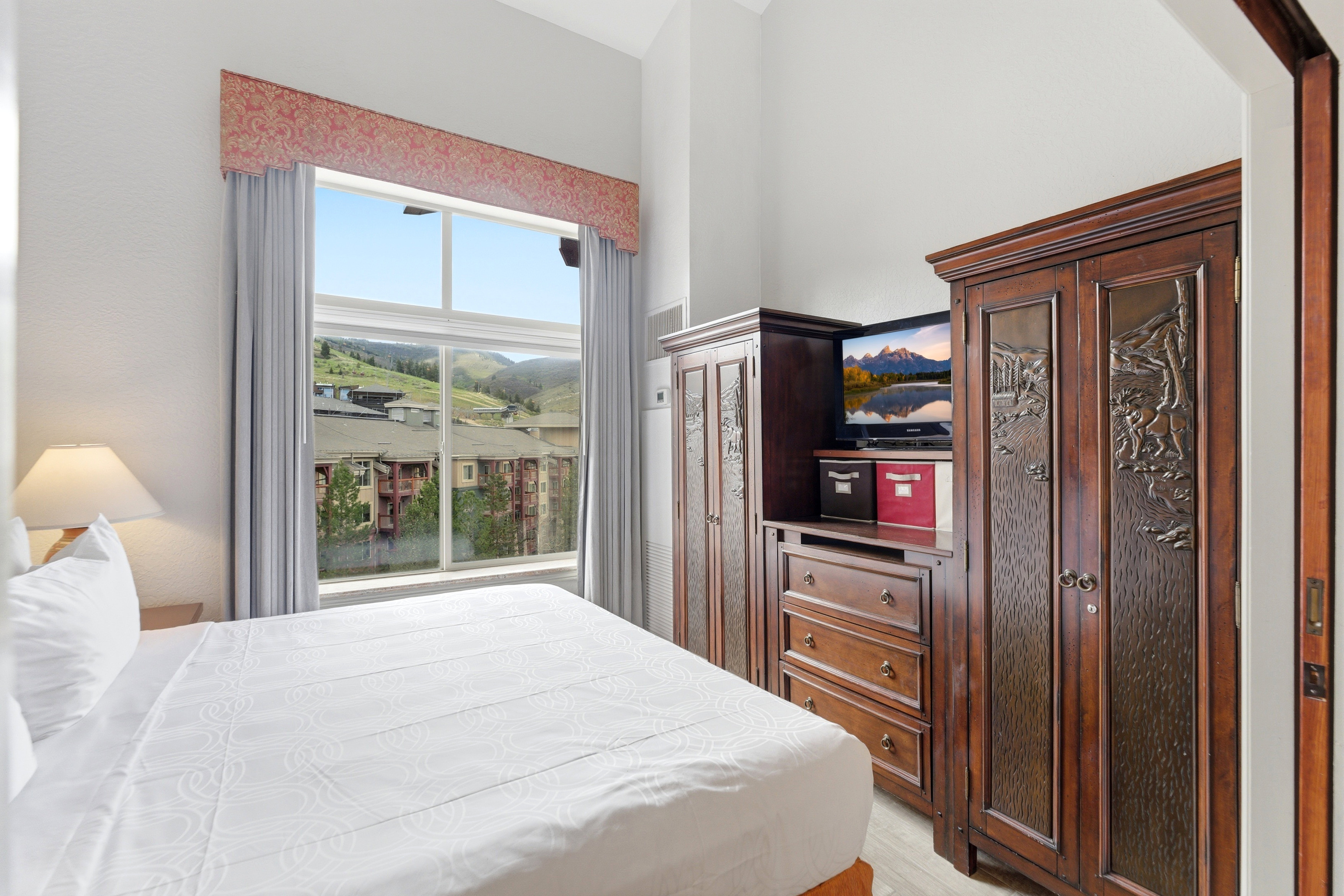 Spacious bedroom with vaulted ceilings, featuring a large window with mountain scenery, light-toned walls, and wood-finish flooring