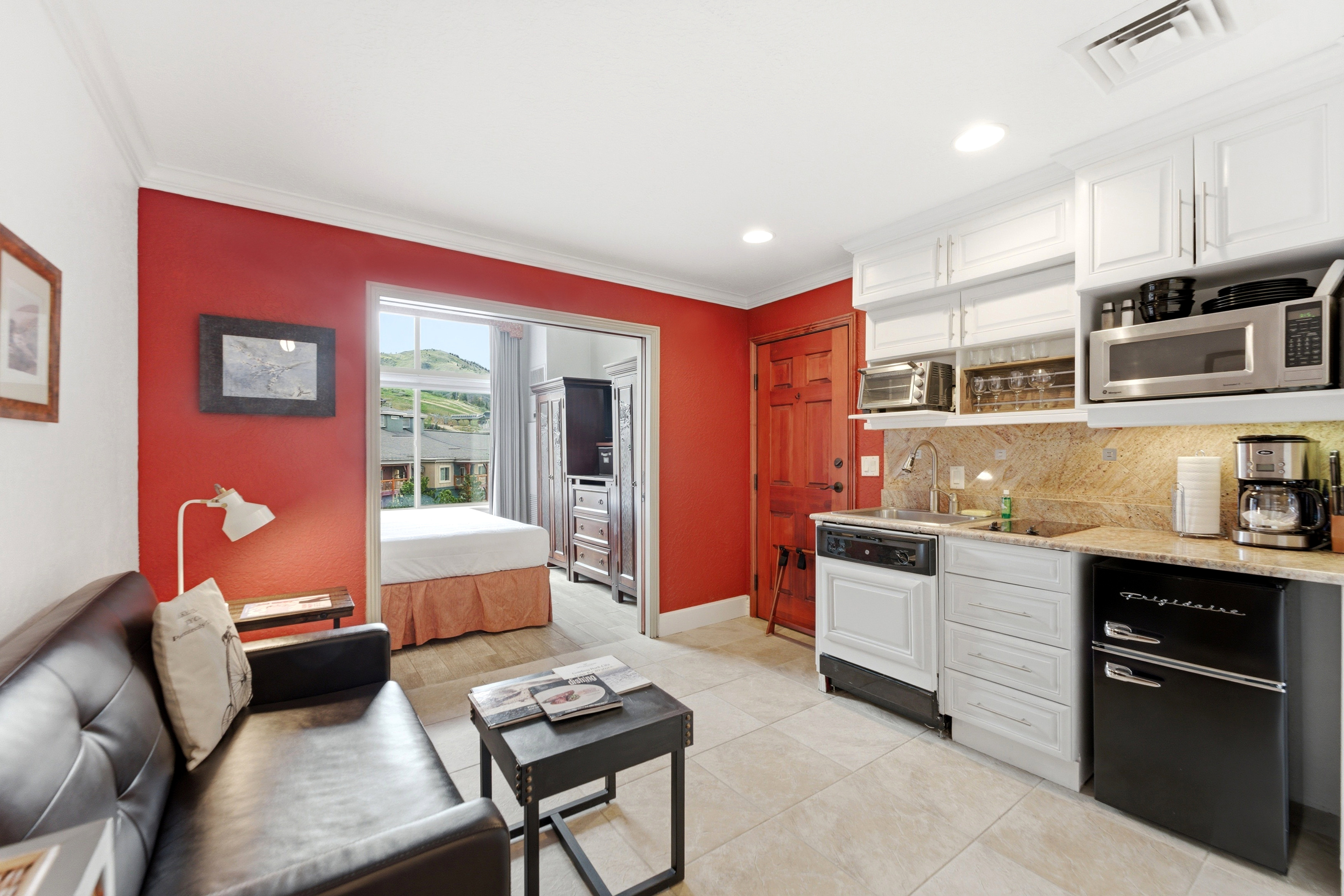 Compact kitchen area featuring white cabinetry, a stone countertop with a matching backsplash, and integrated appliances including a dishwasher and compact refrigerator