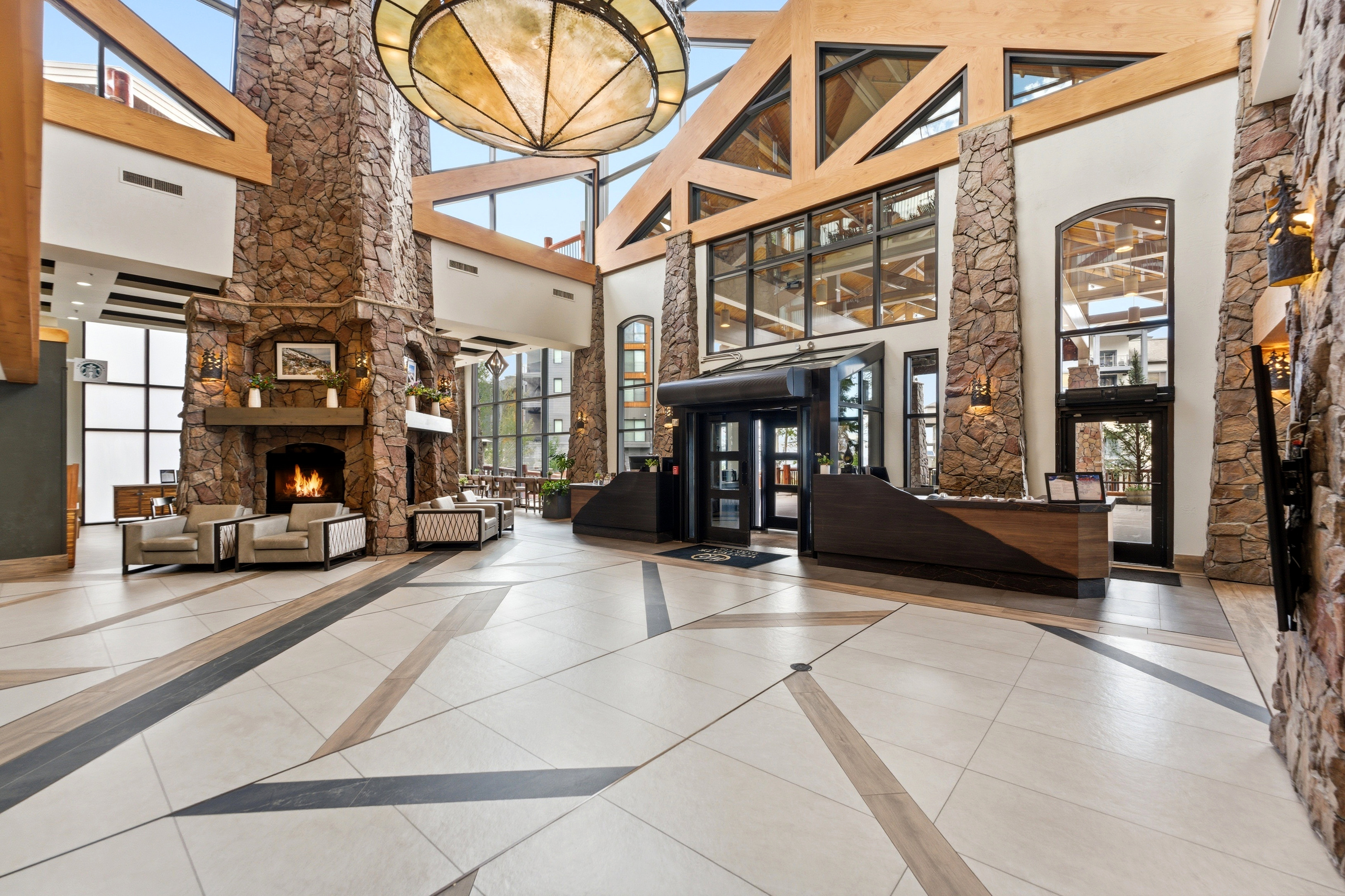 Grand entry with a stone fireplace, exposed timber beams, and a large central chandelier