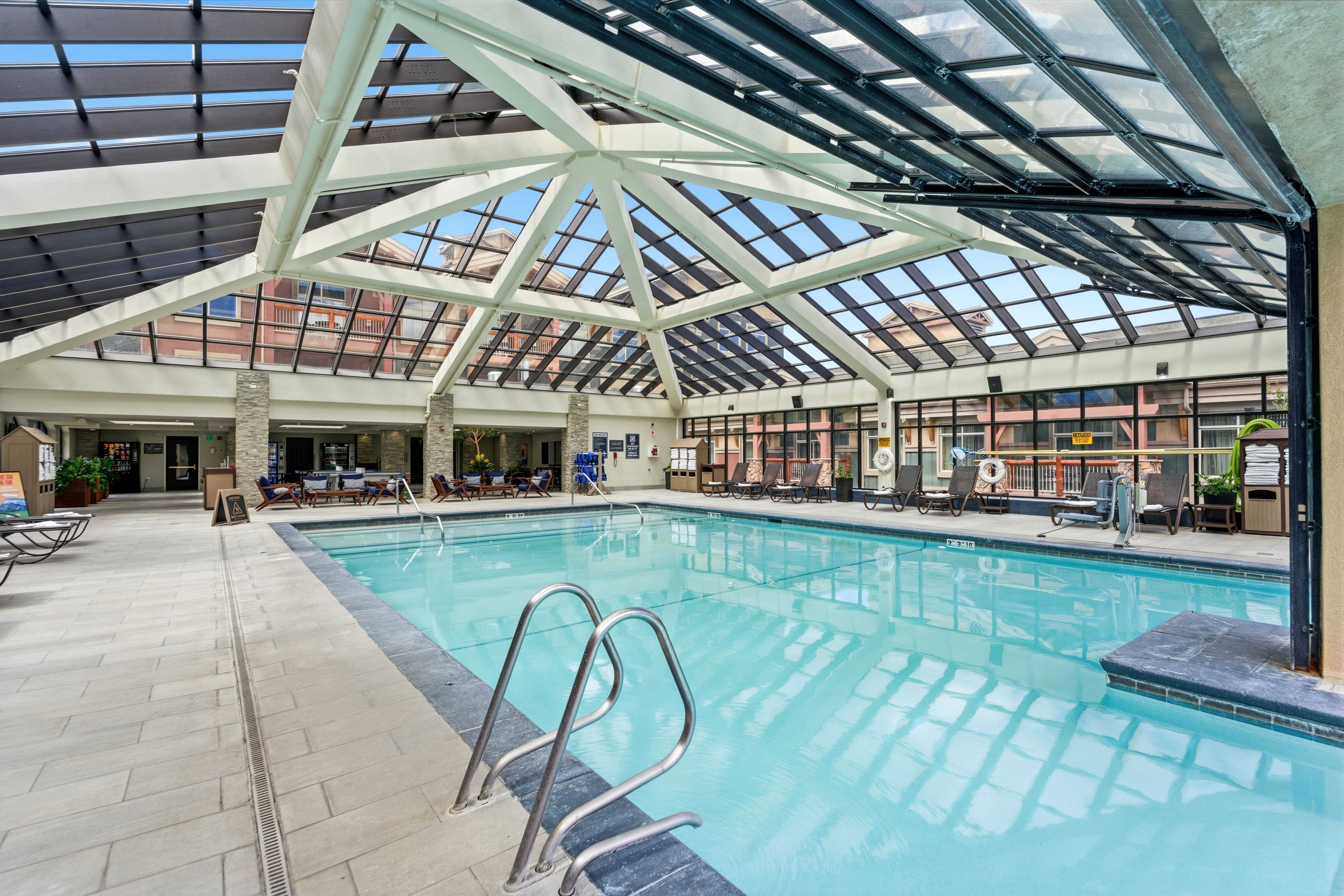 Indoor swimming pool featuring a glass-paneled ceiling, multiple sets of pool stairs, and a surrounding tiled deck