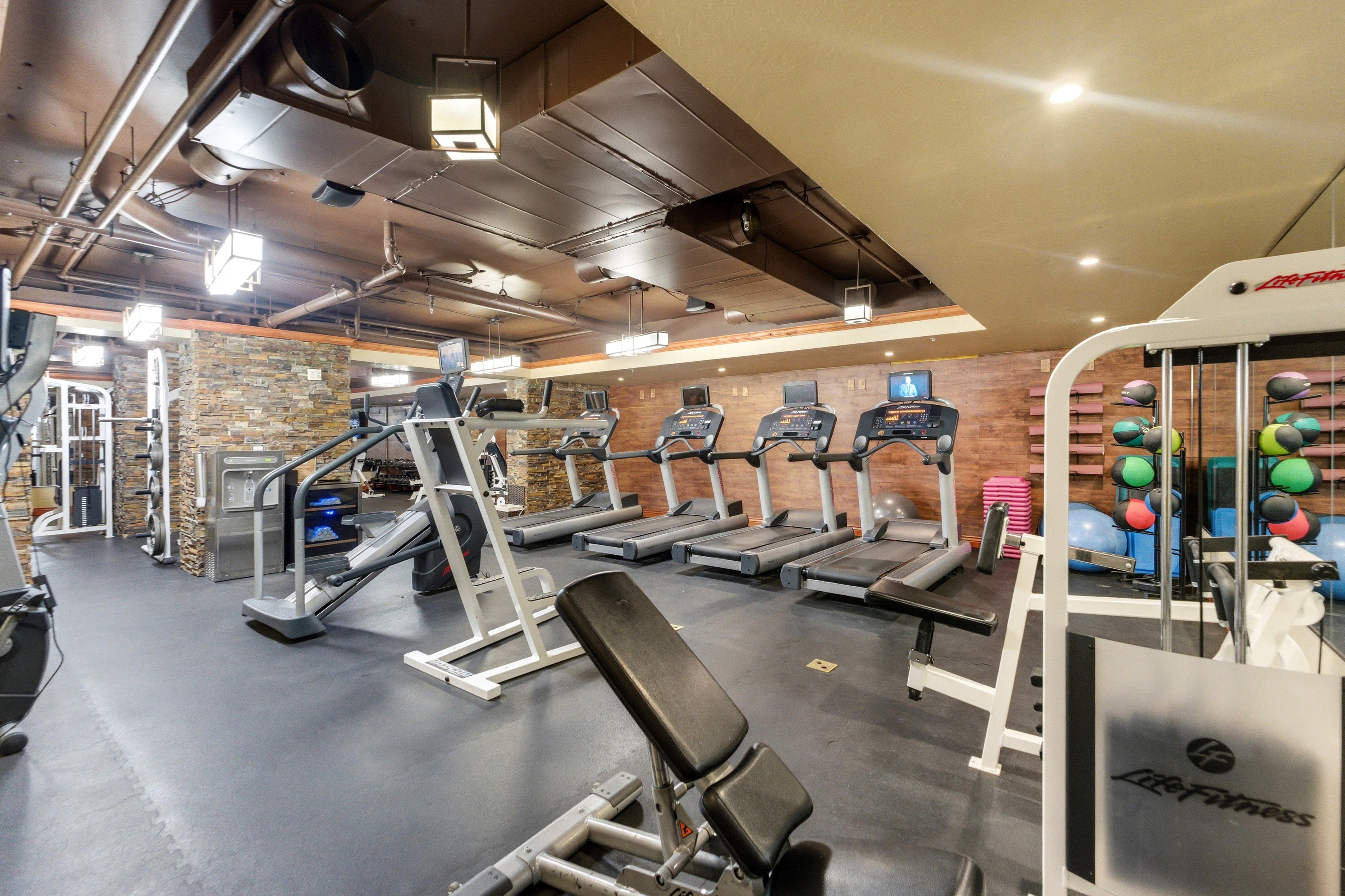 Dedicated fitness space featuring rubber flooring, exposed industrial ductwork, and accent brick walls
