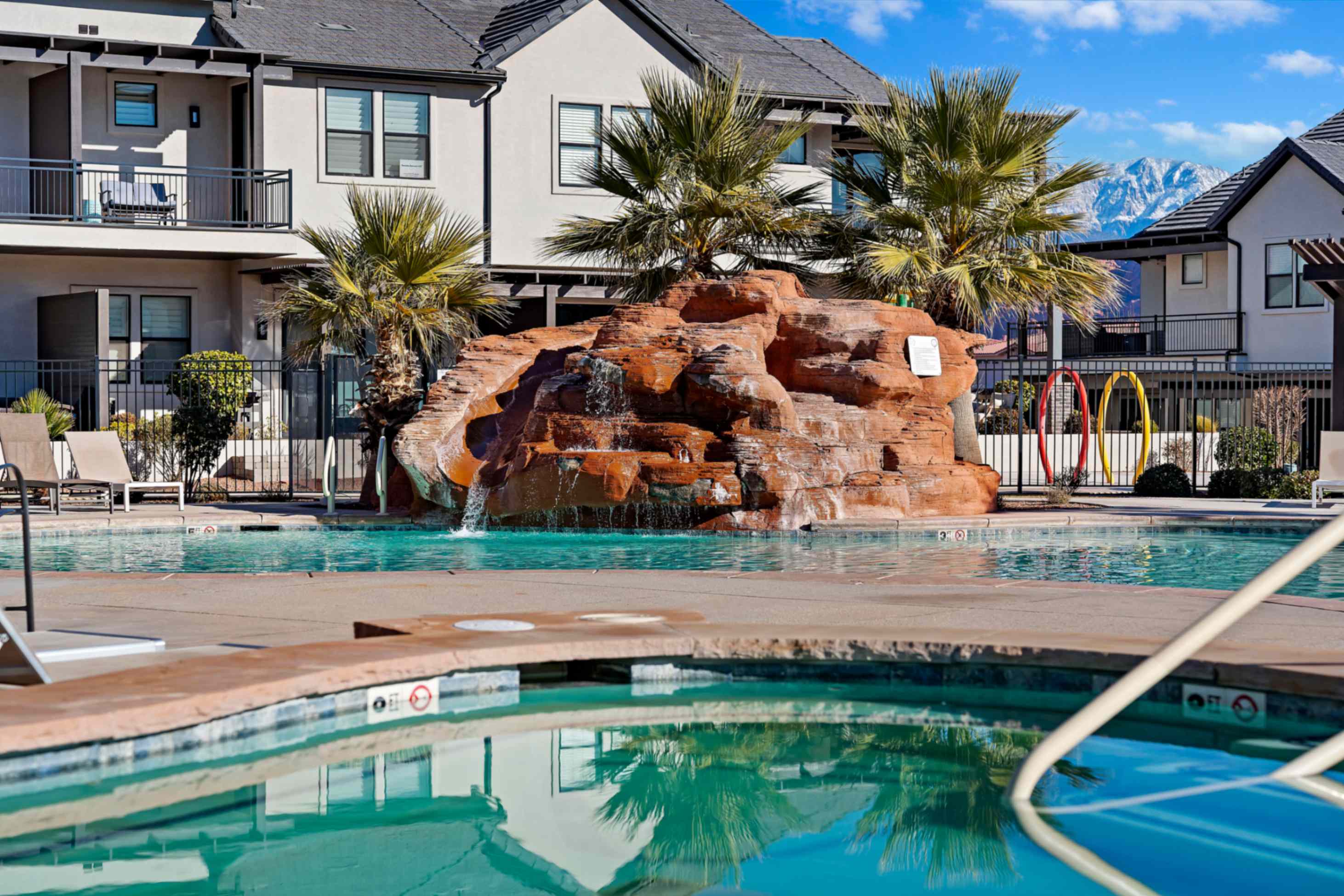 Resort-style pool area featuring a rock-like waterfall, integrated spa, and surrounding palm trees