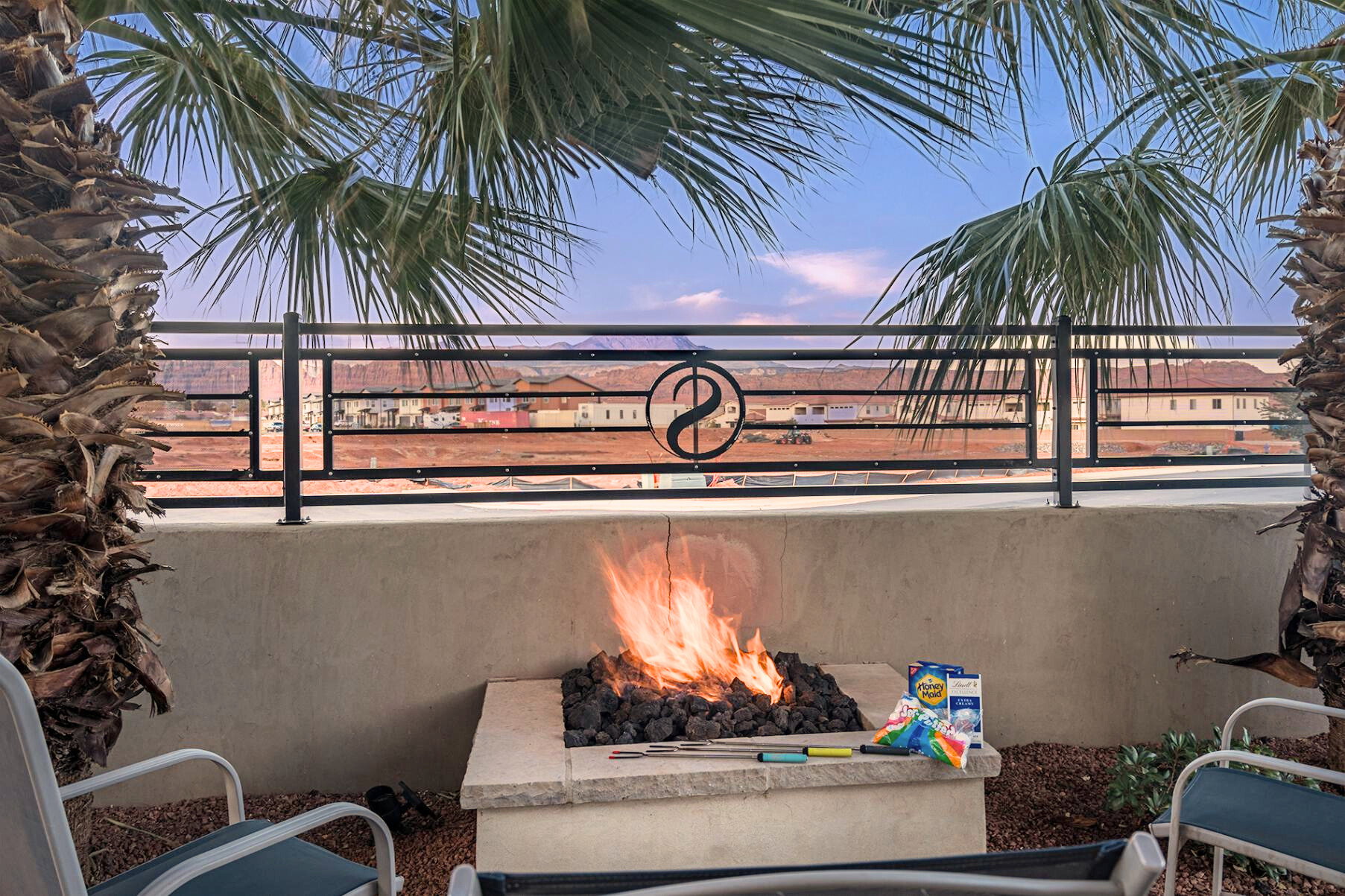 Outdoor patio featuring a built-in fire pit with lava rocks, framed by mature palm trees