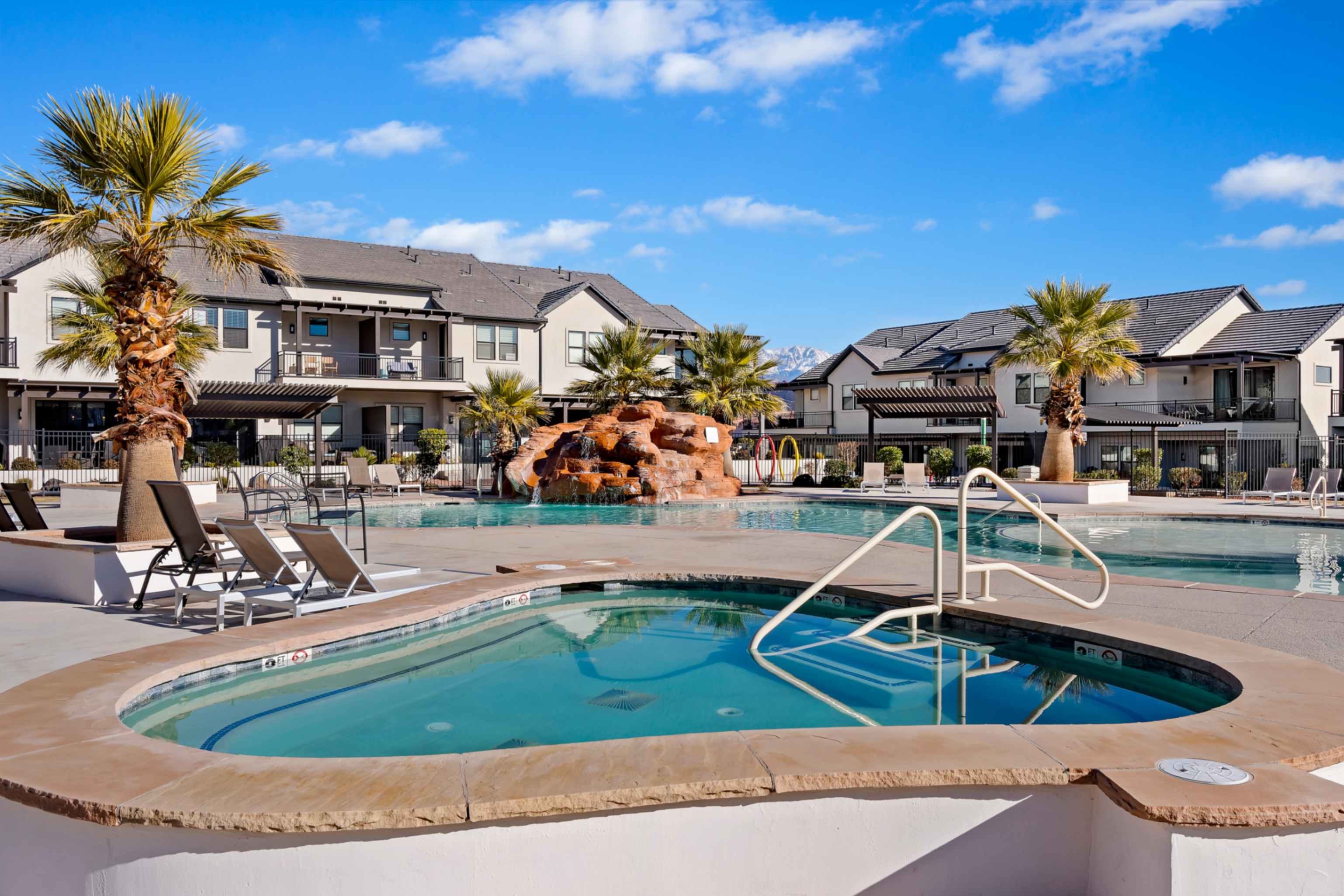 Resort-style pool area featuring a curved spa, expansive swimming pool, decorative rock waterfall, and mature palm trees