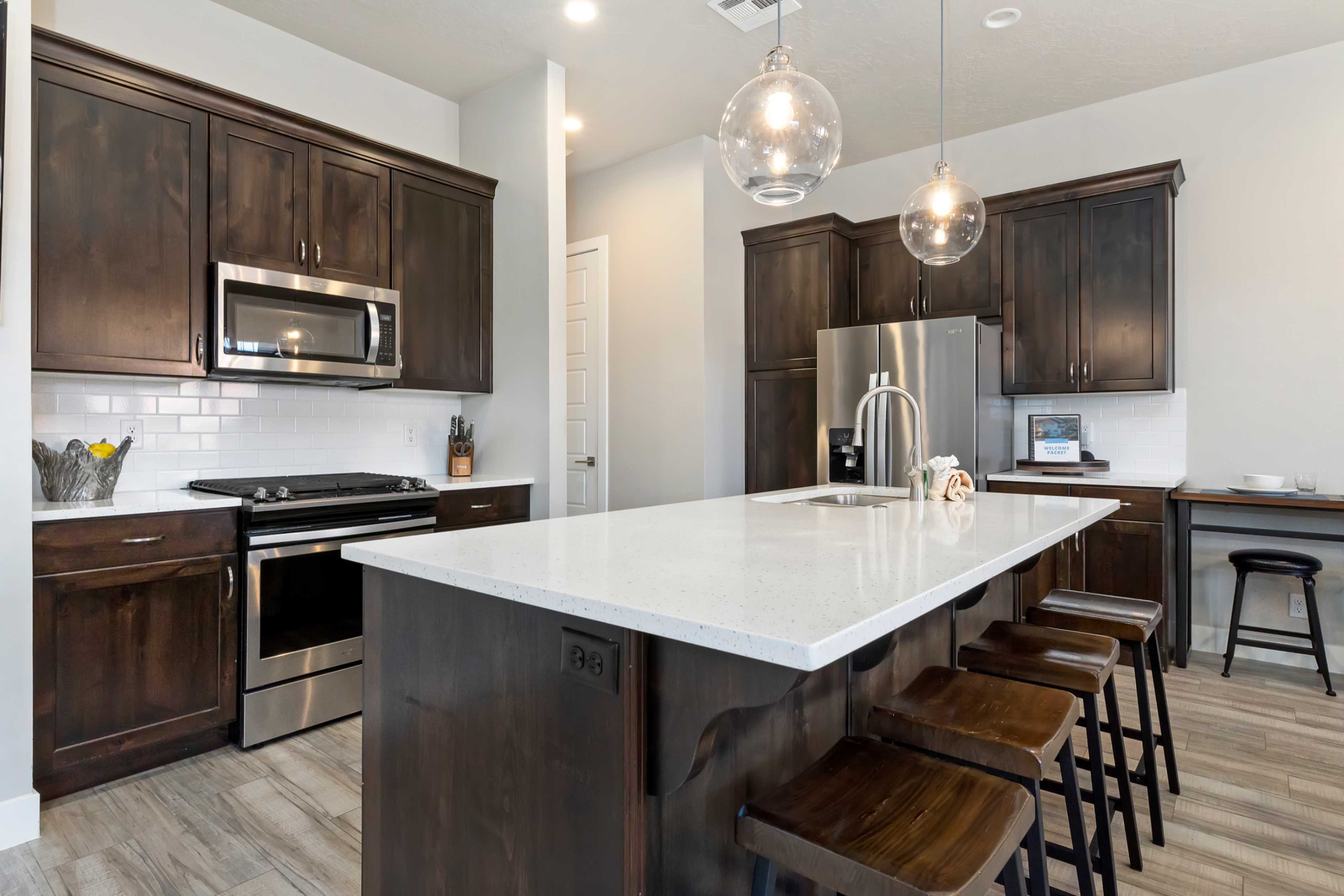 Kitchen featuring a large central island with a light-toned countertop, dark wood-finish cabinetry, stainless steel appliances, a white subway tile backsplash, and wood-look flooring