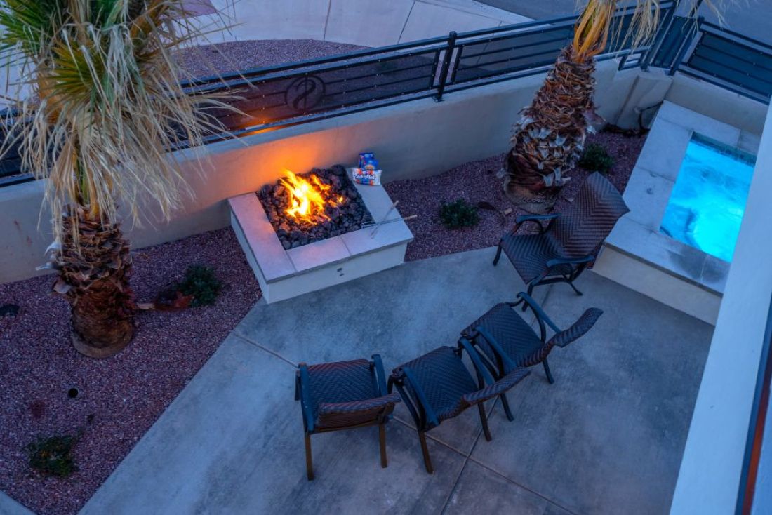 Outdoor patio featuring a built-in fire pit, a spa with blue lighting, and mature palm trees