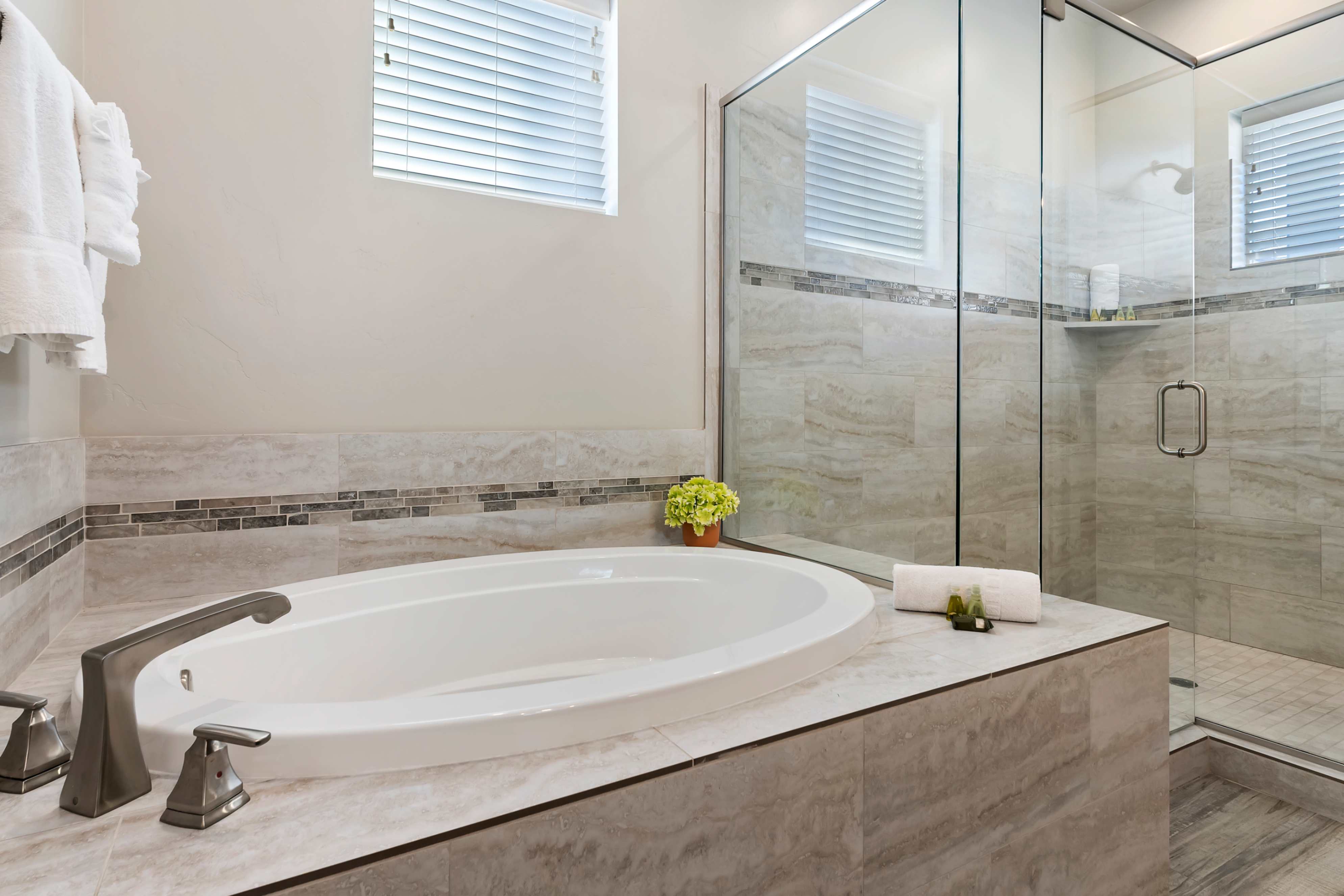 Soaking tub with brushed nickel fixtures, complemented by a glass-enclosed shower with a built-in shelf
