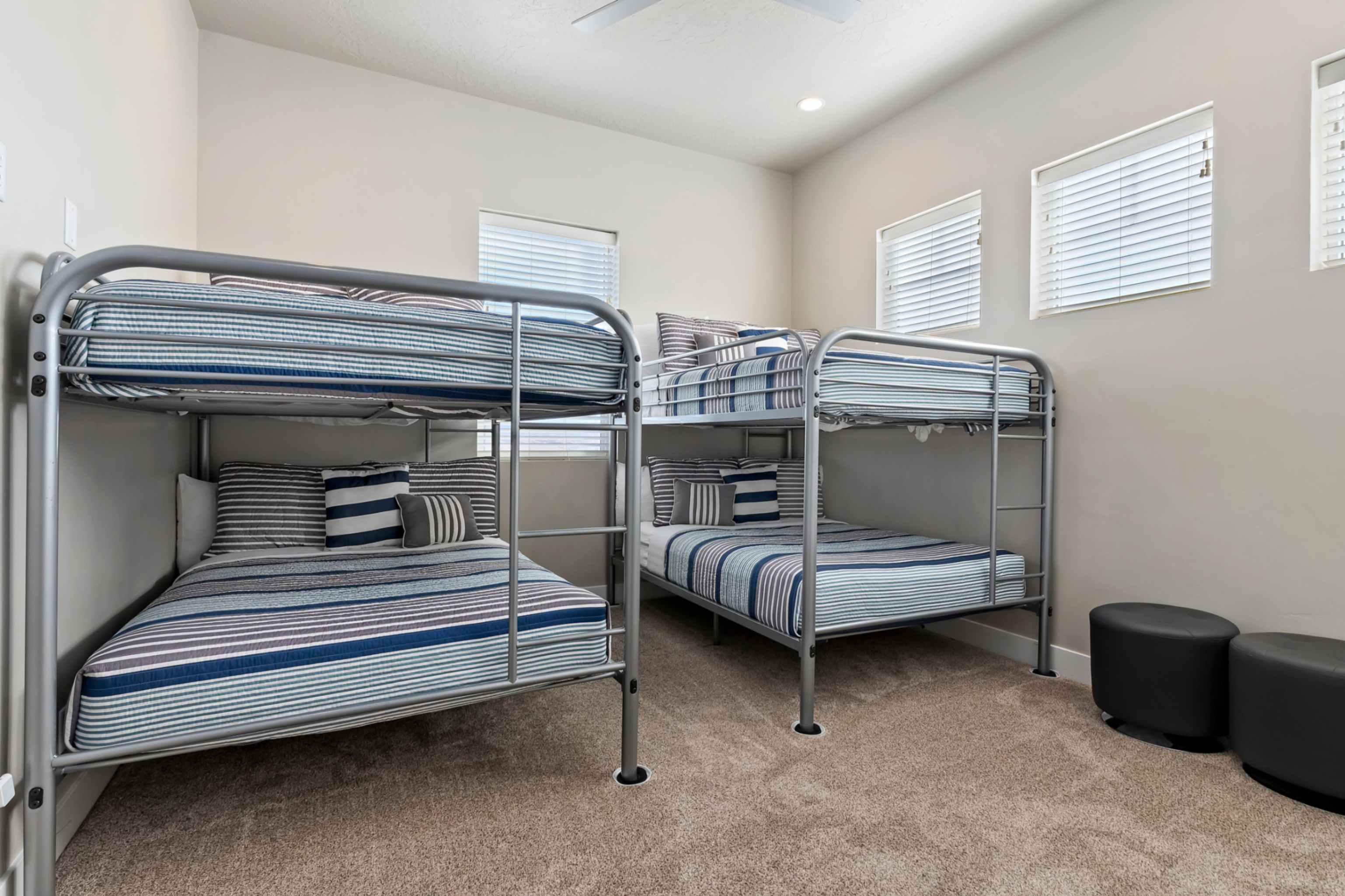 Carpeted room featuring two bunk beds with metal frames, multiple windows with blinds, and a ceiling fan