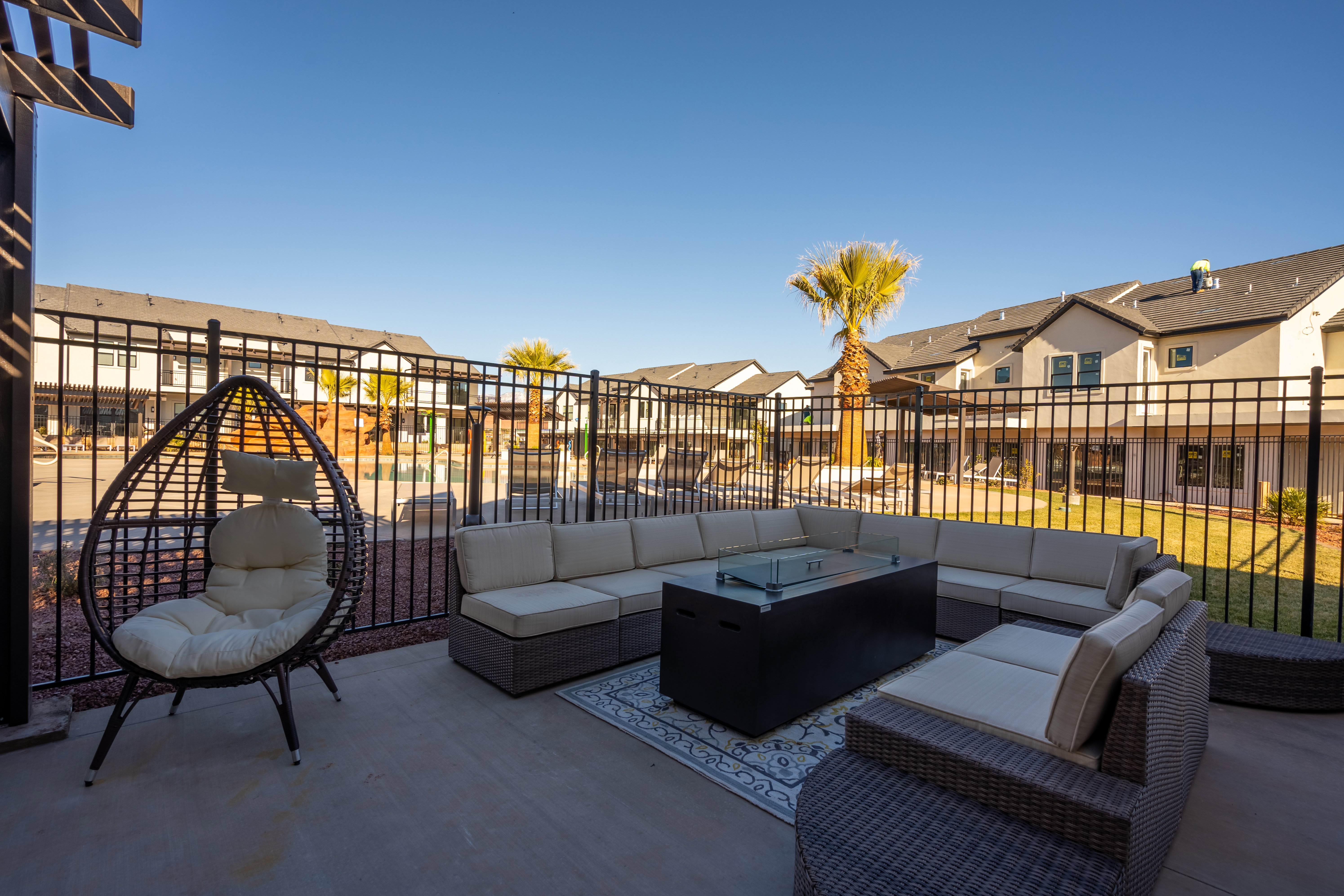 Spacious concrete patio featuring a black metal fence, a decorative pergola element, and partial views of surrounding properties