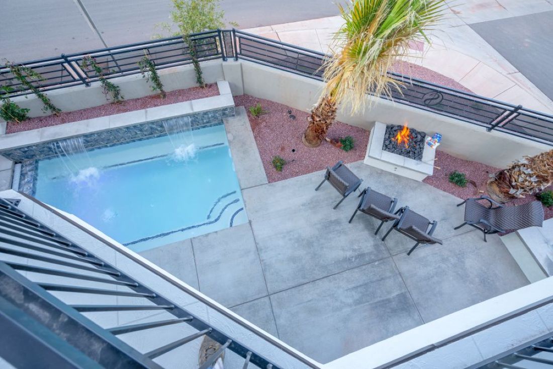 Outdoor patio featuring a rectangular swimming pool with waterfall features, a built-in fire pit, and concrete hardscaping