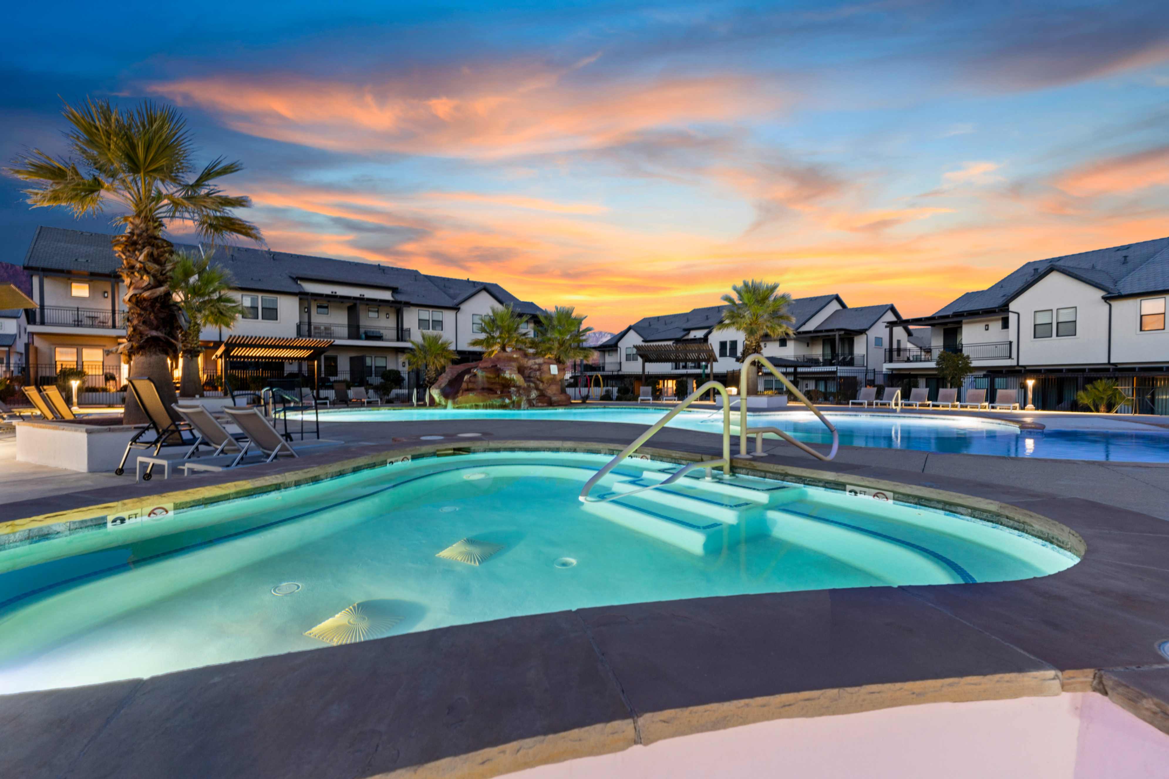 Resort-style pool area featuring a large swimming pool, integrated spa with steps and handrails, and tropical landscaping with palm trees