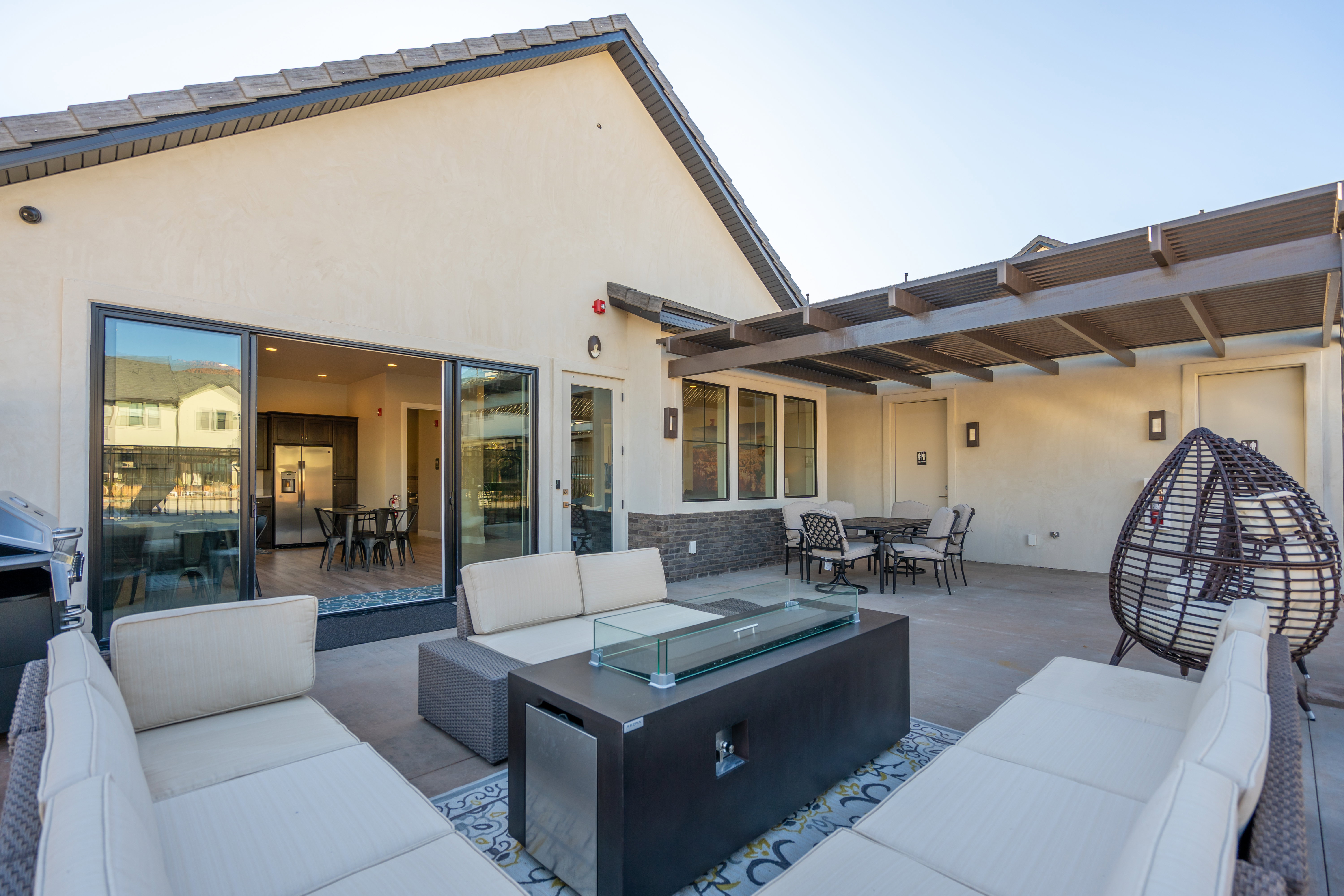 Spacious concrete patio featuring a modern gas fire pit, a partial pergola, and direct access to interior via sliding glass doors