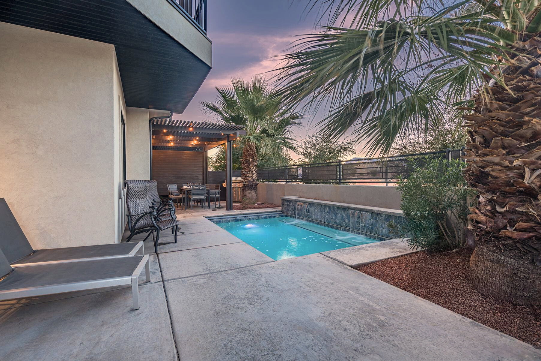 Concrete patio featuring a compact swimming pool with stone-clad waterfall and integrated spa