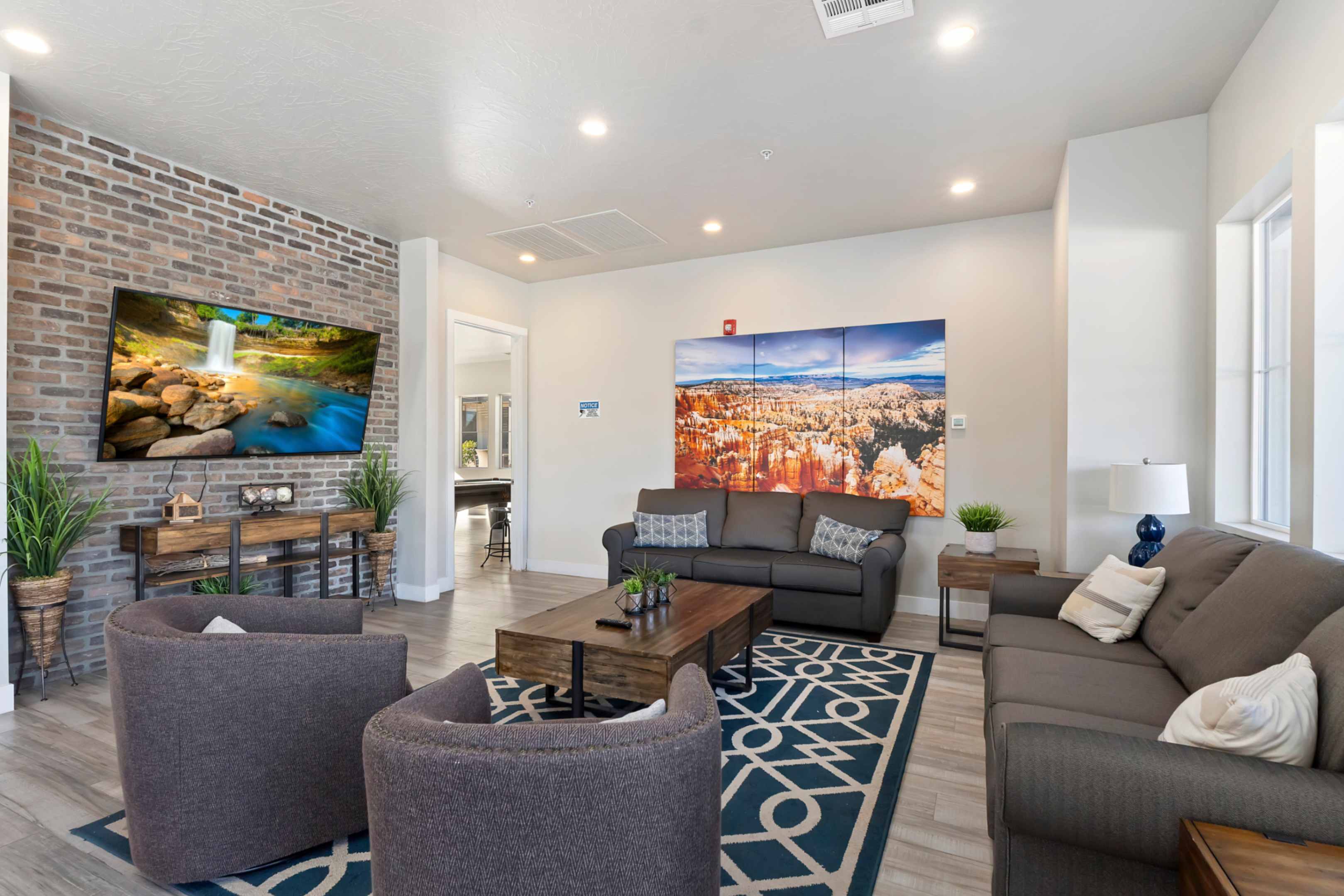 Spacious living area featuring a prominent exposed brick accent wall, recessed lighting, wood-finish flooring, and multiple windows for natural illumination