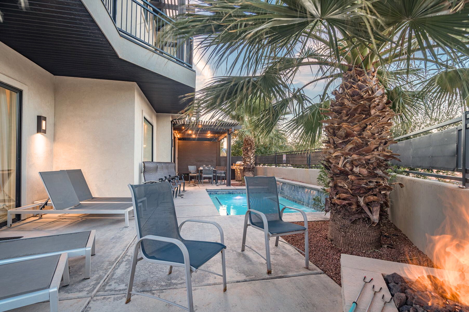 Outdoor living space featuring a private pool with water features, a built-in fire pit, a covered patio with a dining area, a second-story balcony, and mature palm trees