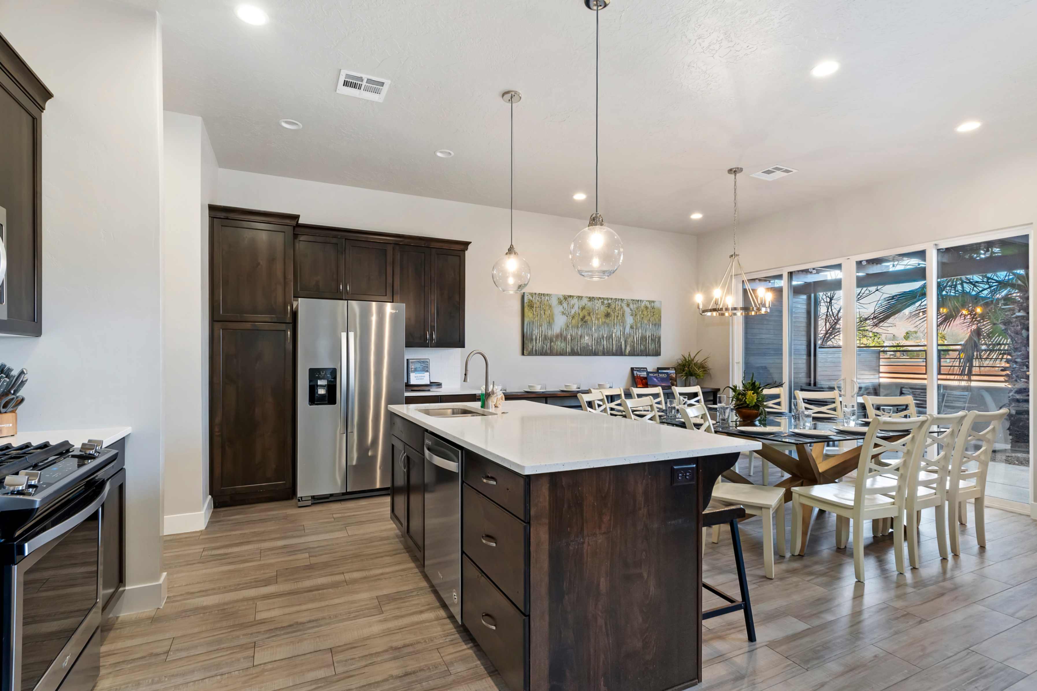 Open-concept kitchen and dining area featuring a central island with a white countertop, dark wood-finish cabinetry, stainless steel appliances, and wood-finish flooring