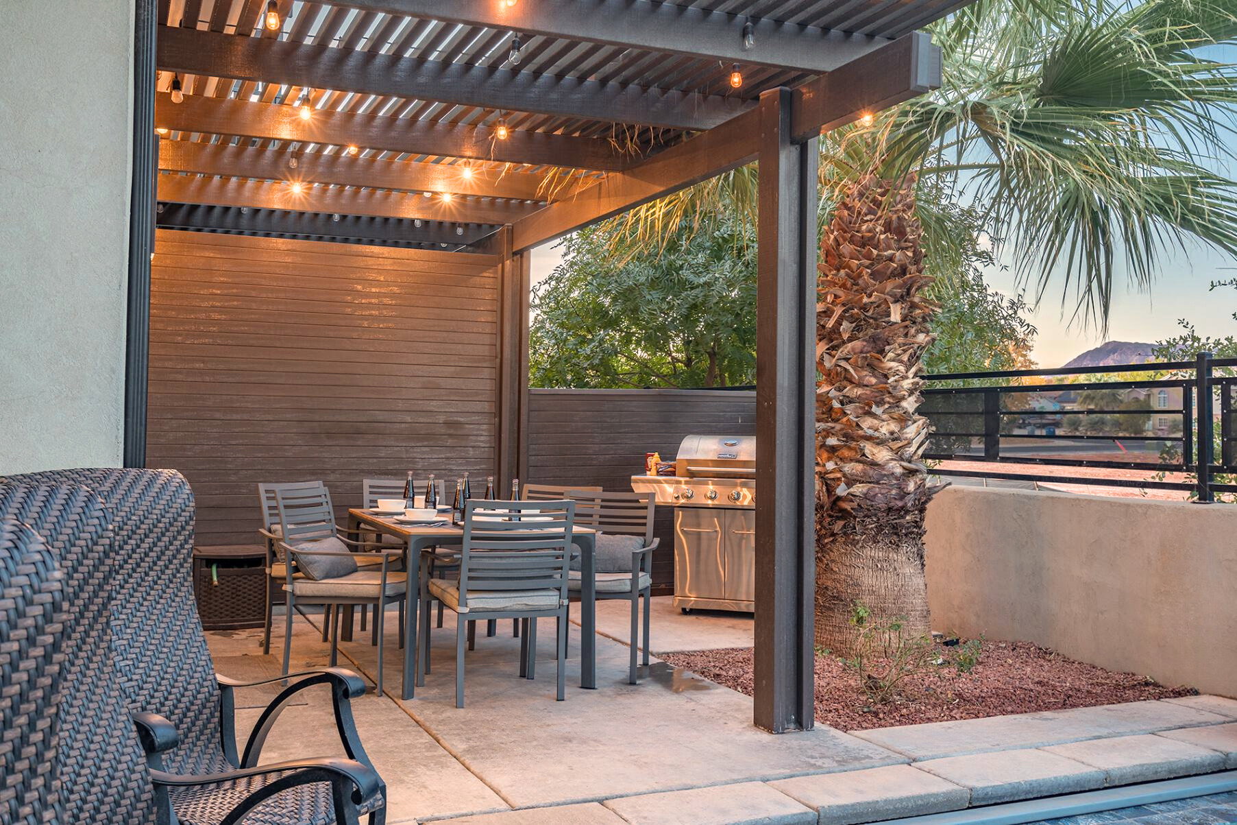 Outdoor patio featuring a dark wood-finish pergola with string lighting, a concrete patio surface, and a stucco retaining wall