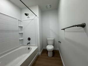 Bathroom featuring a white bathtub and shower surround with built-in shelving, dark bronze fixtures, a white toilet, and wood-finish flooring