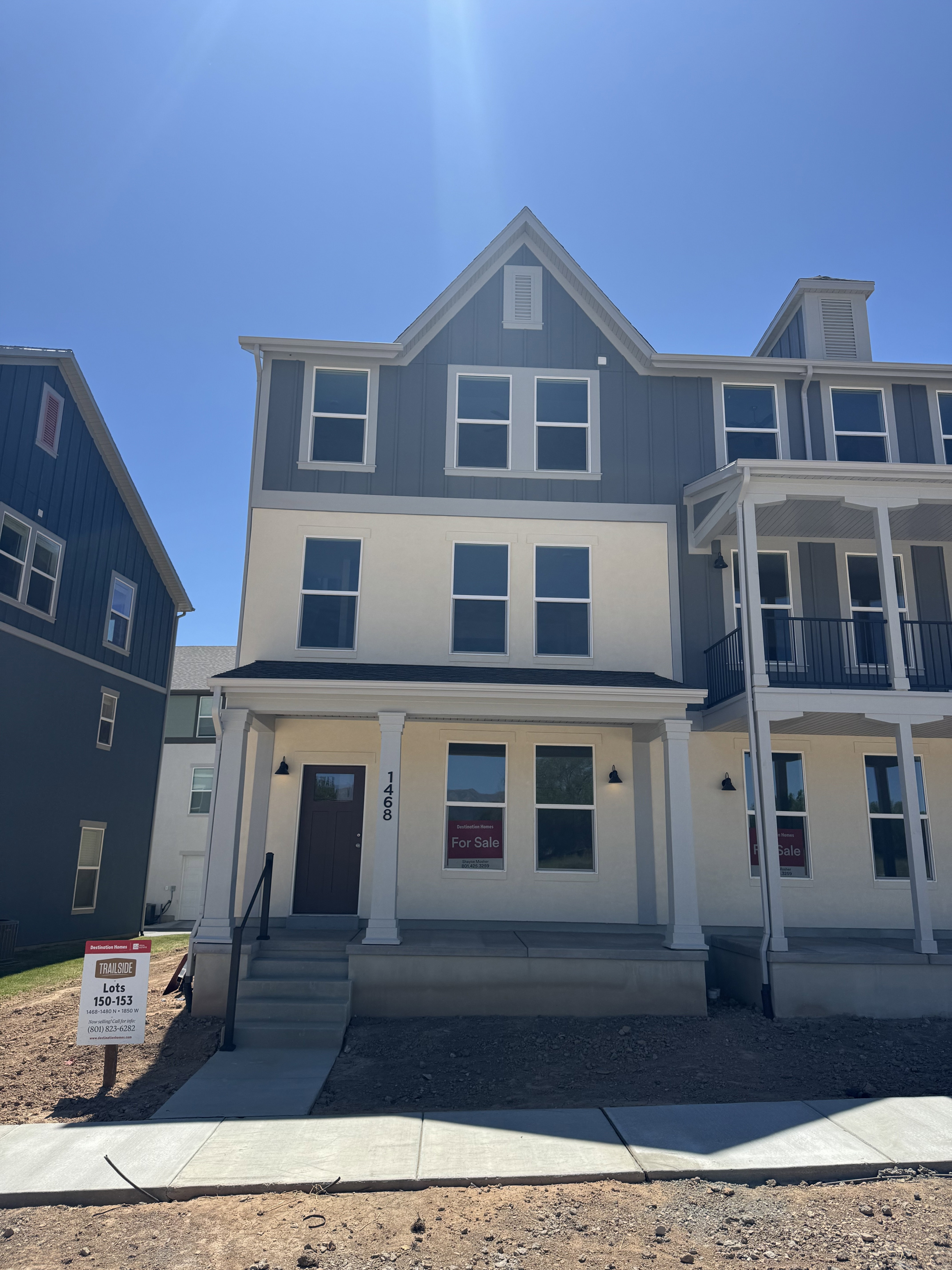 Modern three-story townhouse exterior featuring a covered front porch with columns, a dark brown entry door, and a combination of light-colored stucco and blue vertical siding