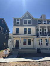 Modern three-story townhouse exterior featuring a covered front porch with columns, a dark brown entry door, and a combination of light-colored stucco and blue vertical siding