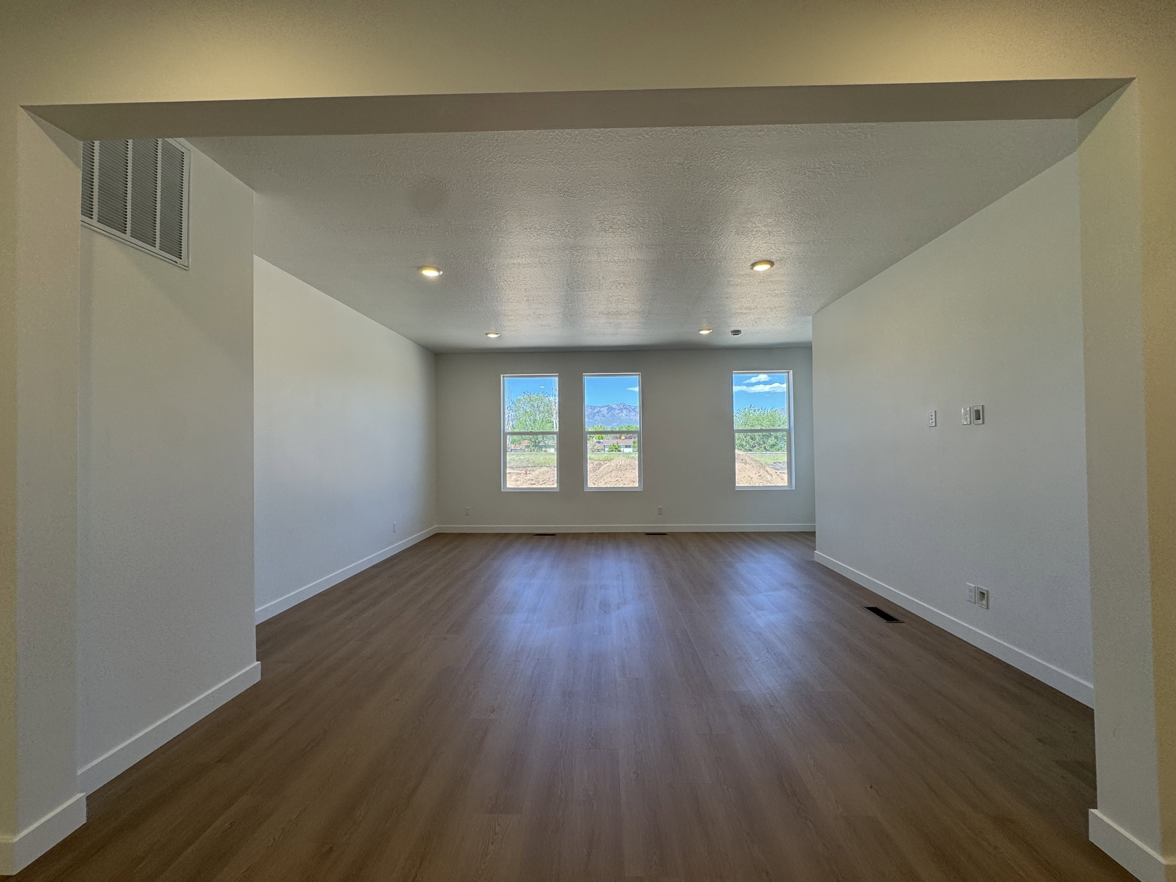 Spacious room with wood-finish flooring, recessed lighting, and three tall windows