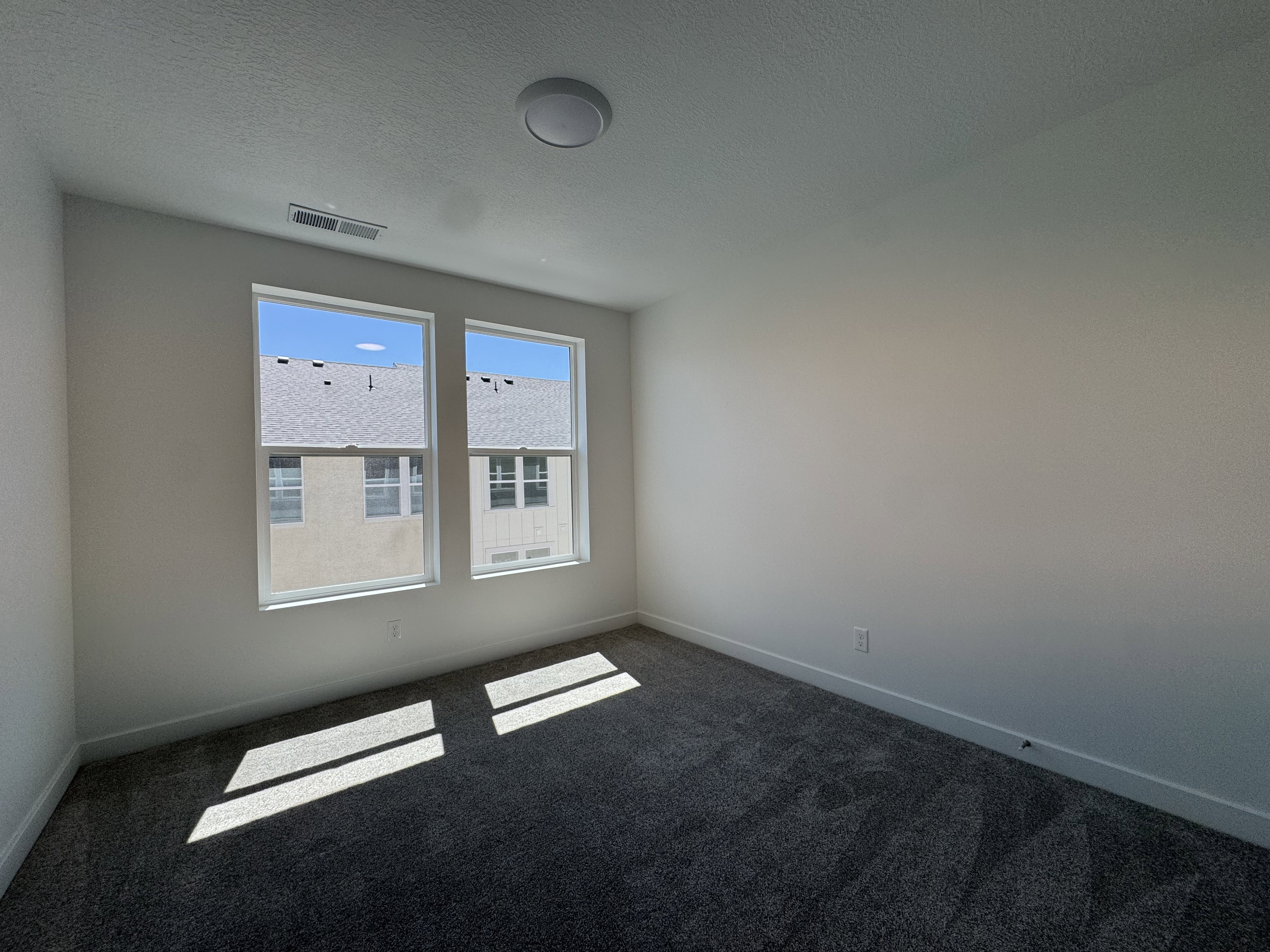 Bedroom featuring two large windows, textured carpeting, white walls, white baseboards, and a flush-mount ceiling light fixture
