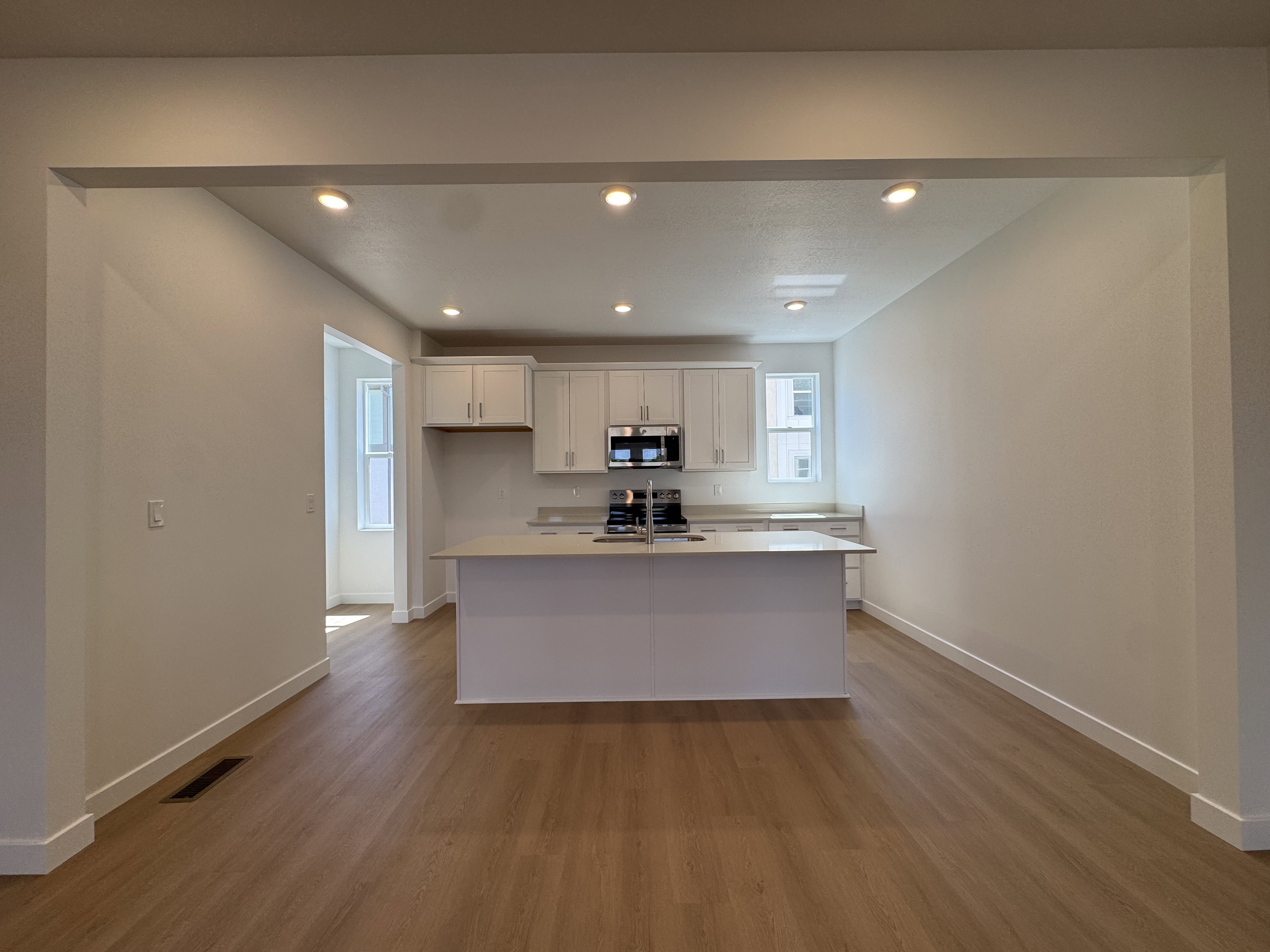 Spacious kitchen featuring white cabinetry, stainless steel appliances, a central island with an undermount sink, recessed lighting, and wood-finish flooring