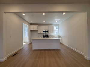 Spacious kitchen featuring white cabinetry, stainless steel appliances, a central island with an undermount sink, recessed lighting, and wood-finish flooring