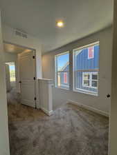 Carpeted hallway with white trim and doors, featuring two windows providing ample natural light