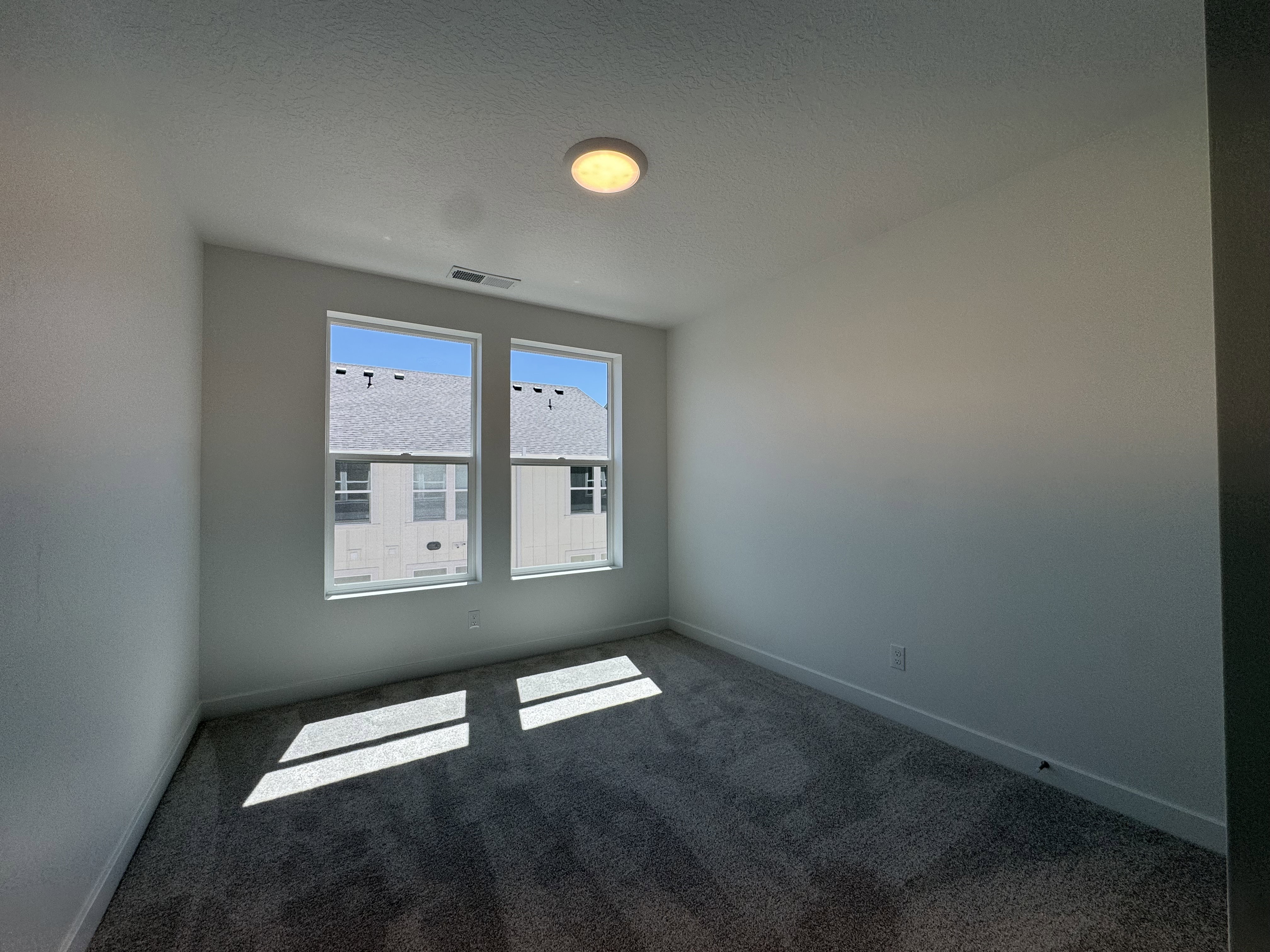 Dual windows providing ample illumination, plush carpet flooring, white painted walls, white baseboards, and a ceiling-mounted light fixture