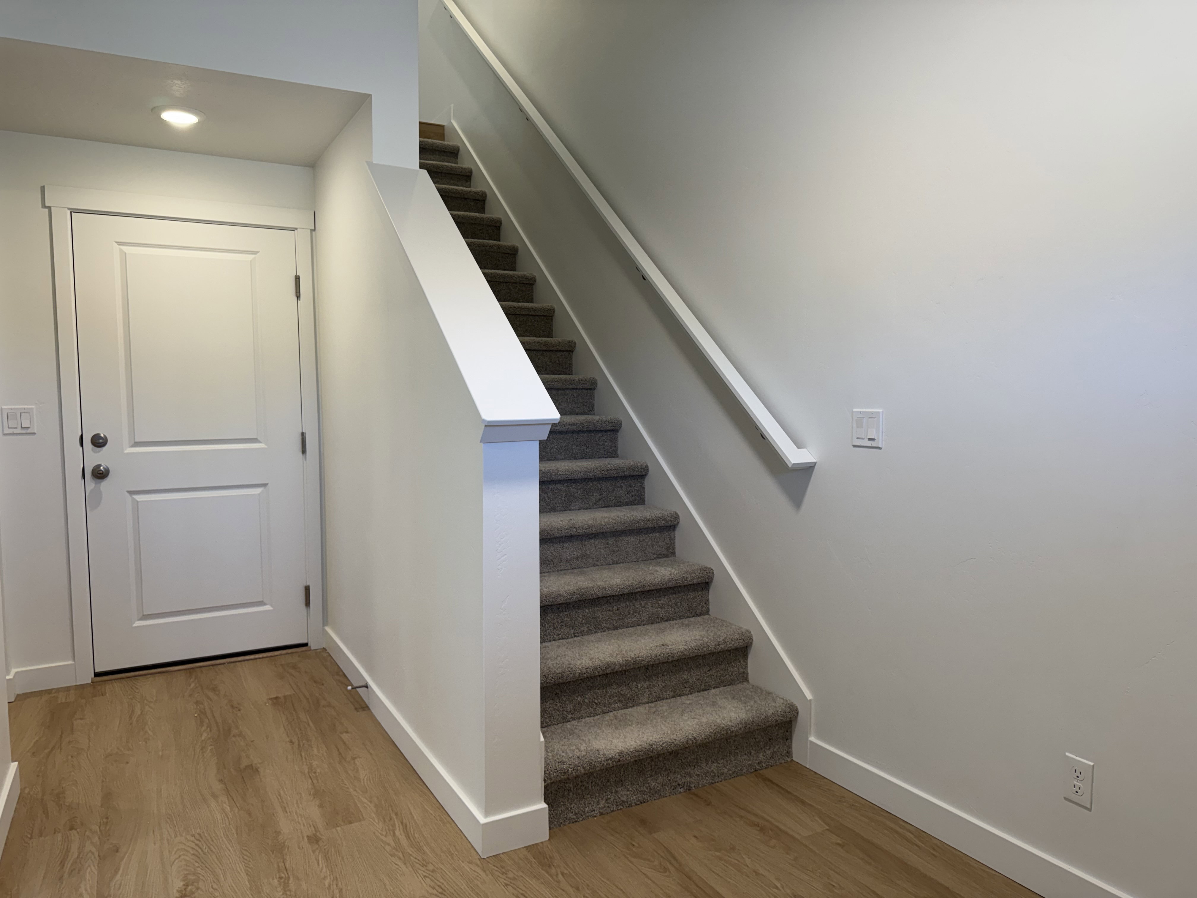 Staircase with carpeted treads and risers, featuring a white handrail and newel post
