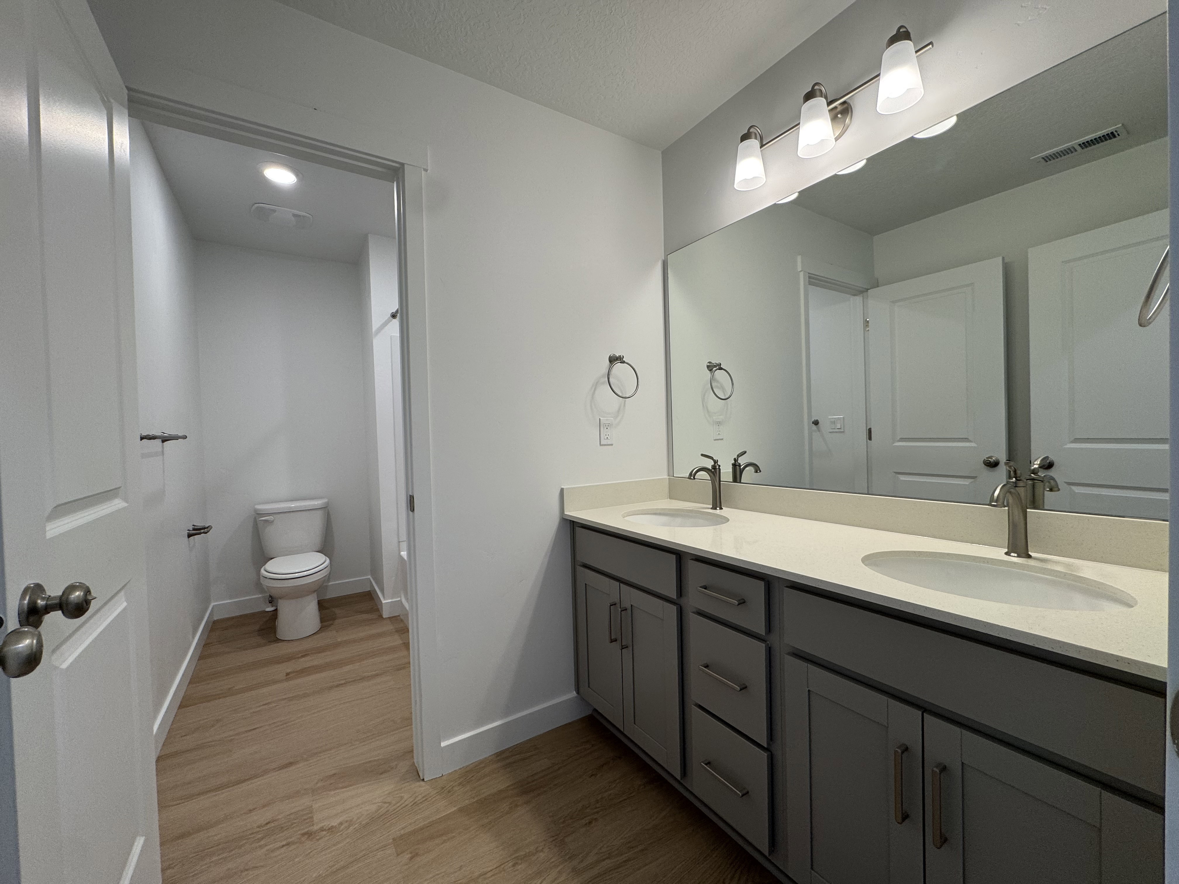 Dual vanity with gray cabinetry and light-toned countertops, featuring chrome fixtures and a wide mirror
