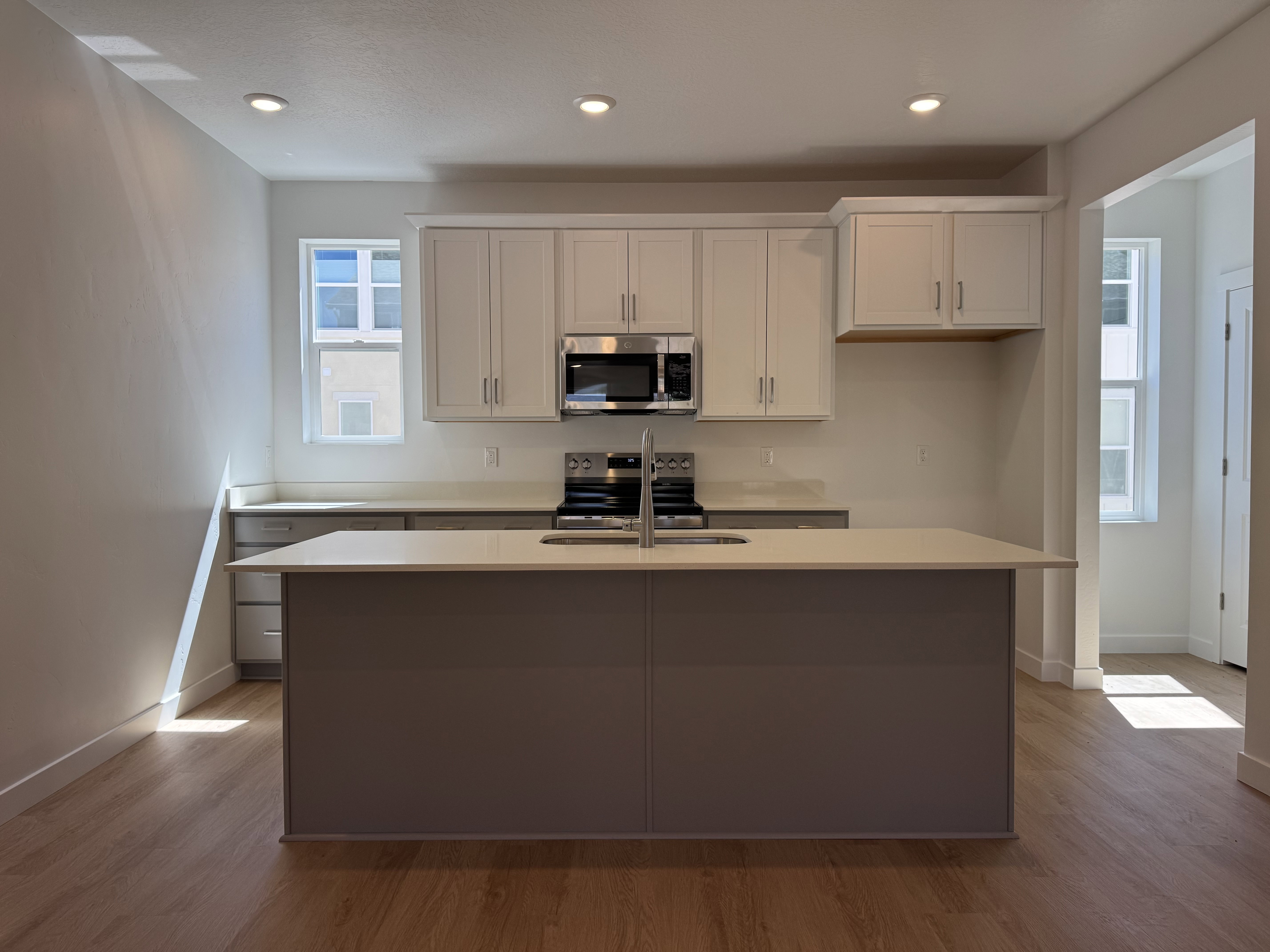 Modern kitchen featuring a central island with an undermount sink, light-toned countertops, and white upper cabinetry