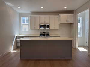Modern kitchen featuring a central island with an undermount sink, light-toned countertops, and white upper cabinetry
