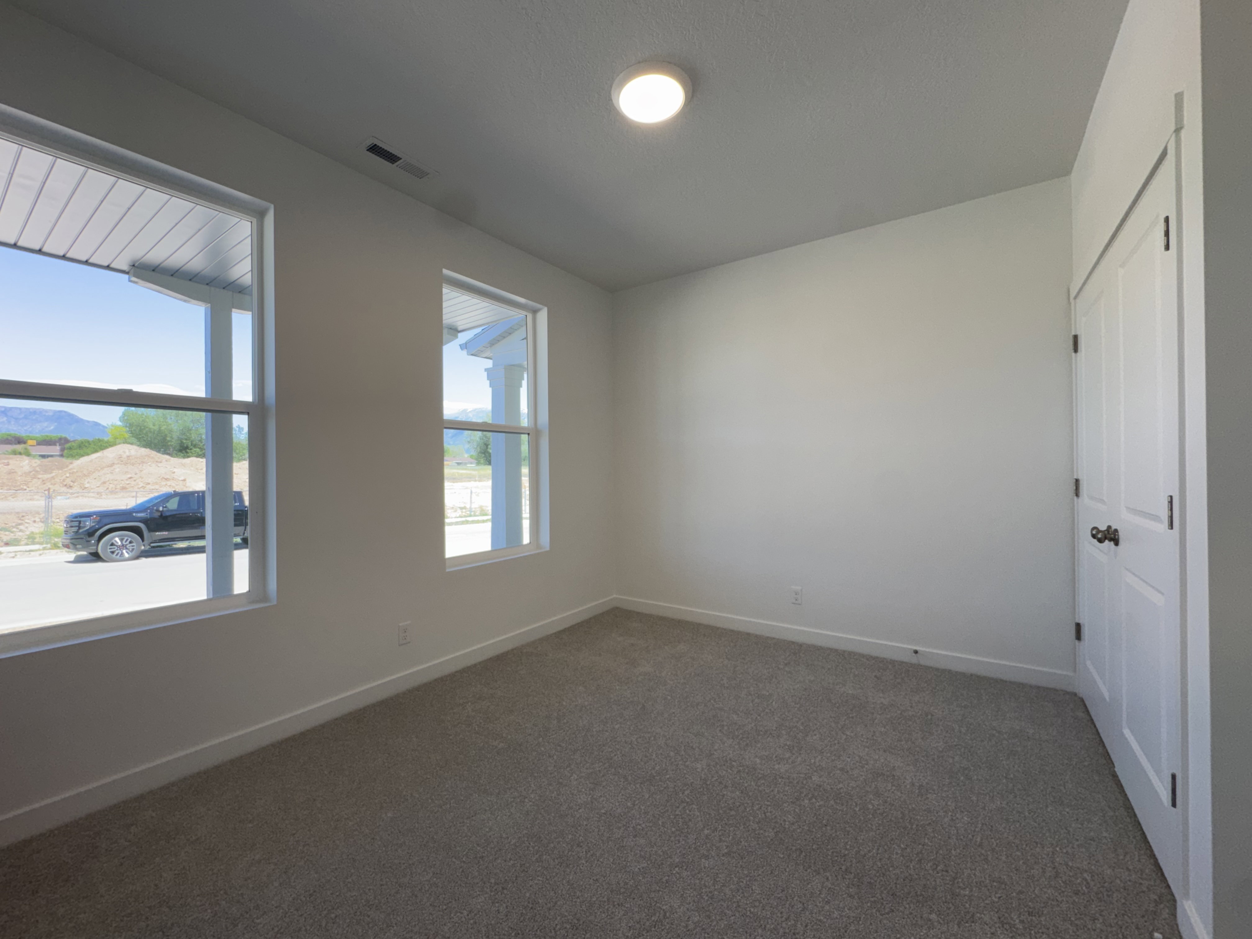 Carpeted room featuring two large windows, white walls, and a white paneled door
