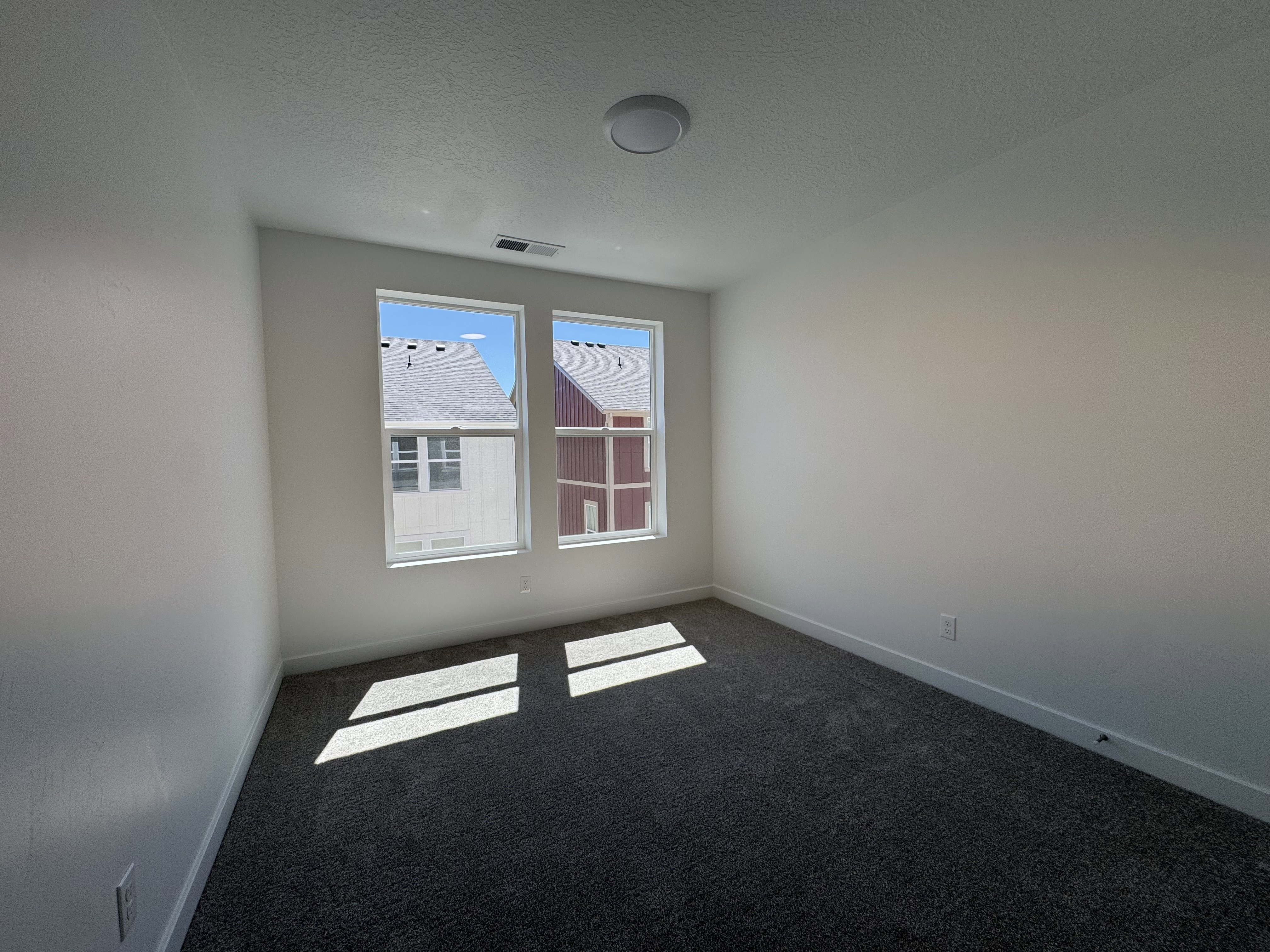 Bright interior room with two large windows, white walls, and dark gray carpet flooring