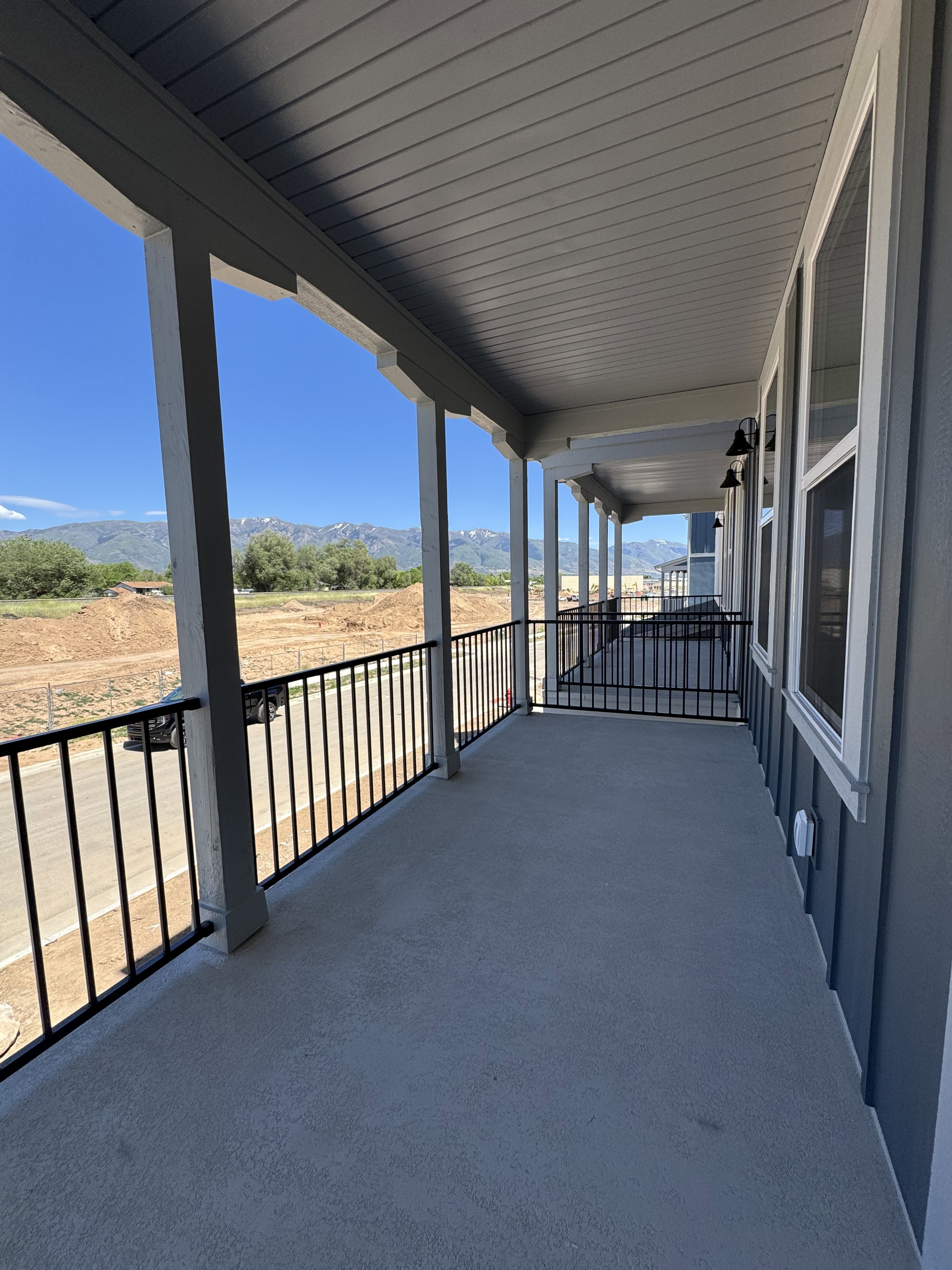 Covered outdoor balcony featuring mountain scenery, concrete flooring, black metal railings, and attached exterior lighting