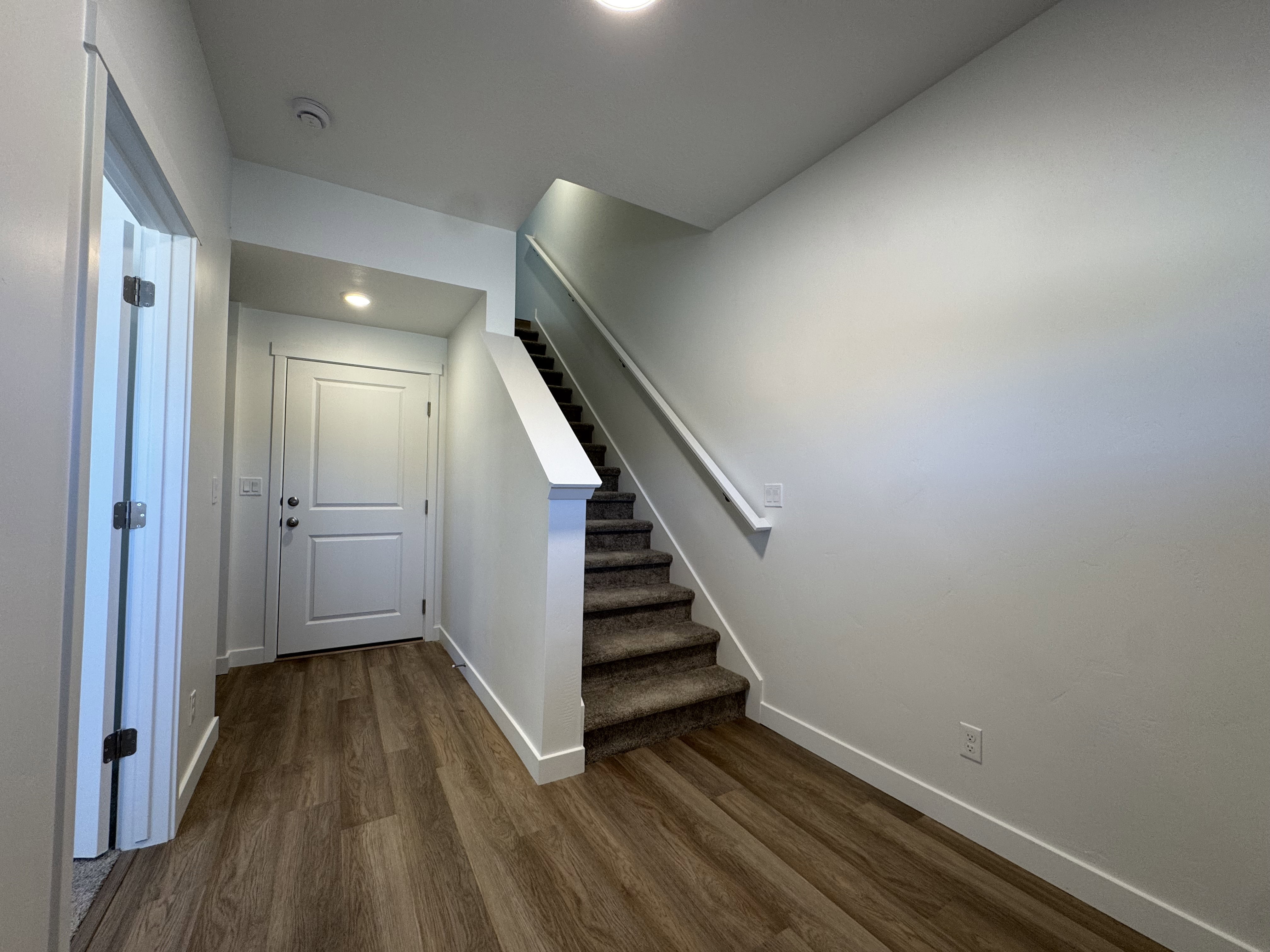 Entryway featuring wood-finish flooring, a two-panel door with hardware, recessed lighting, and a carpeted staircase with a white handrail