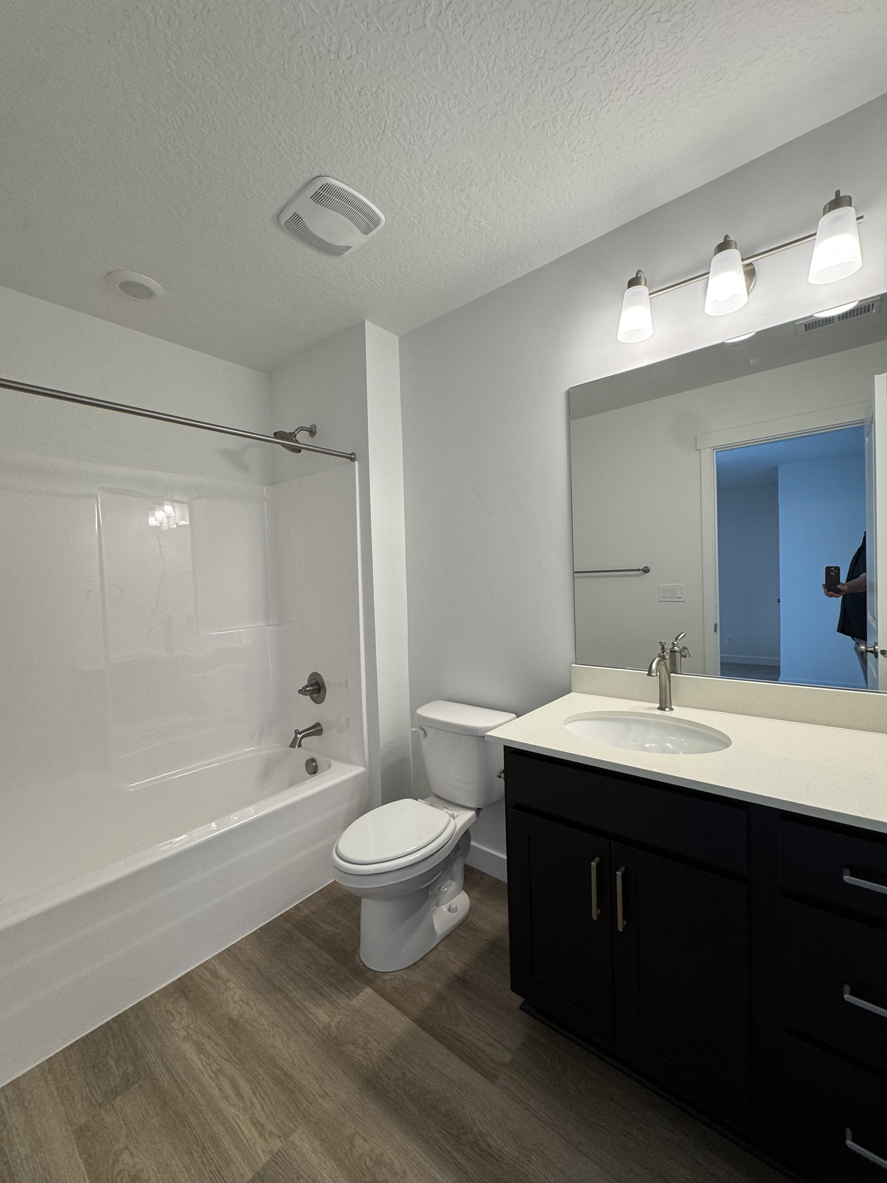 Contemporary bathroom featuring a dark wood-finish vanity with a light countertop, a rectangular mirror, and a white tub/shower combination