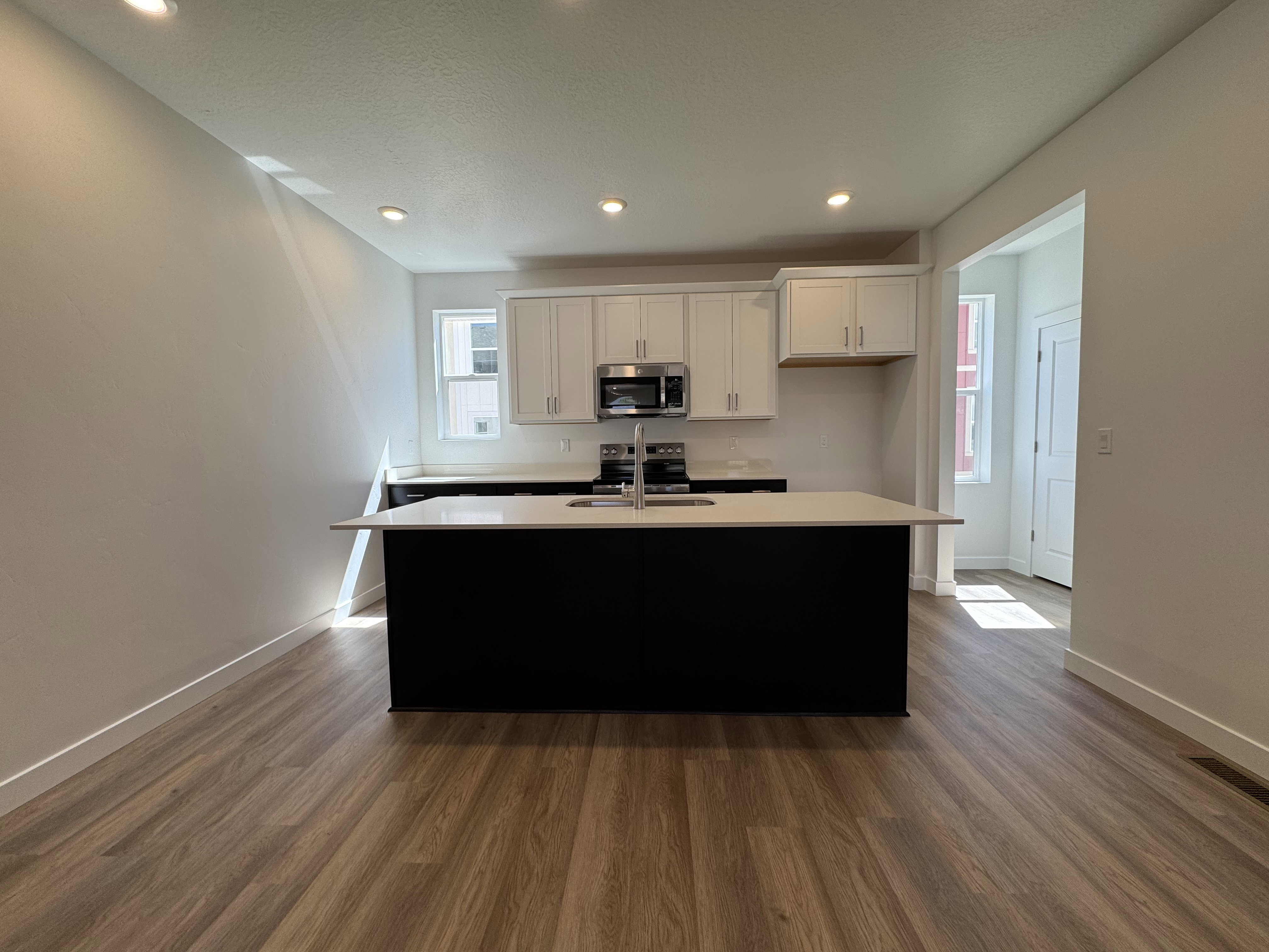 Open-concept kitchen featuring an island with counter seating, stainless steel appliances, white cabinetry, and wood-finish flooring