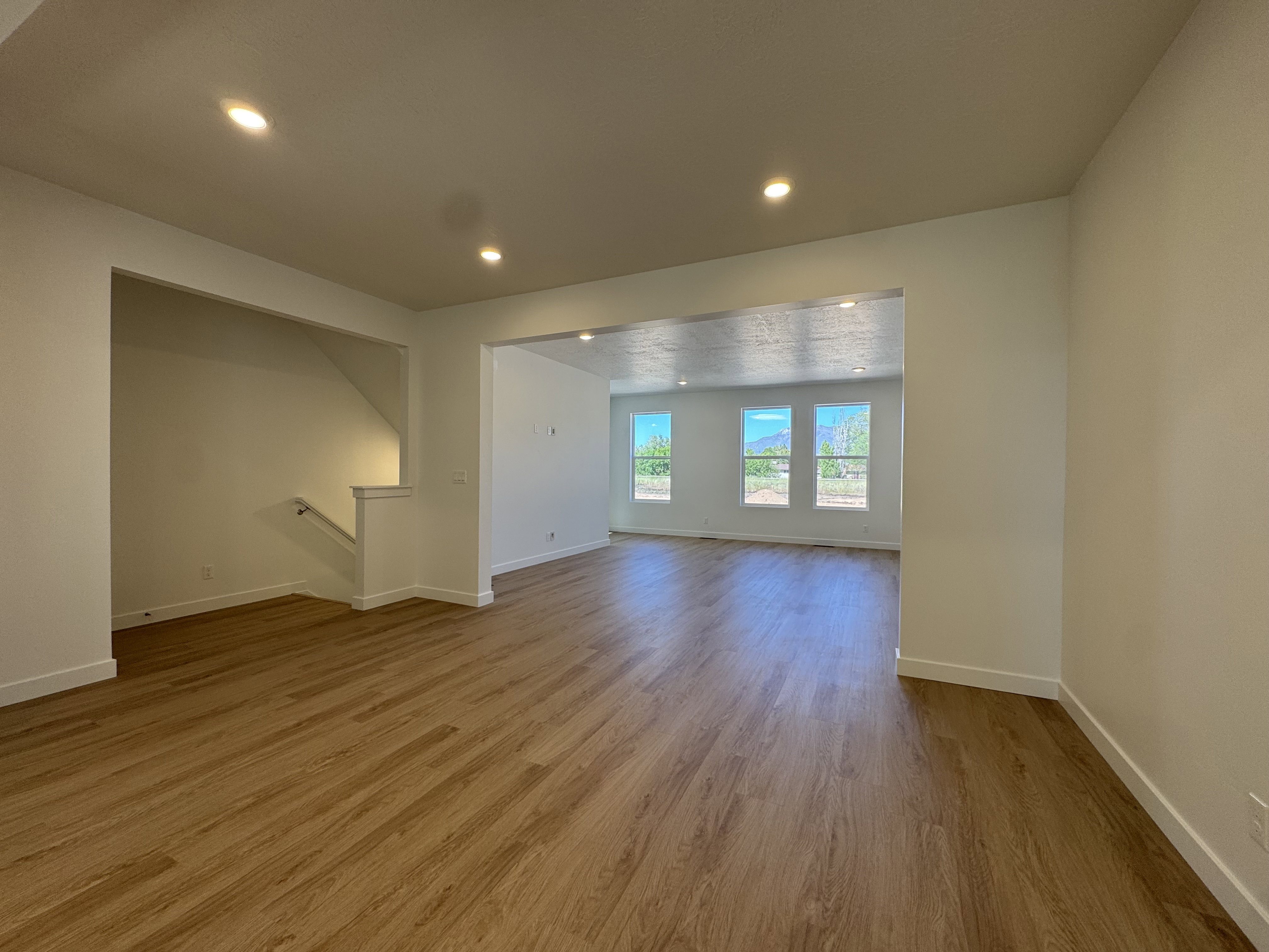 Expansive interior featuring wood-finish flooring, recessed lighting, white baseboards, a staircase with a white railing, and multiple windows