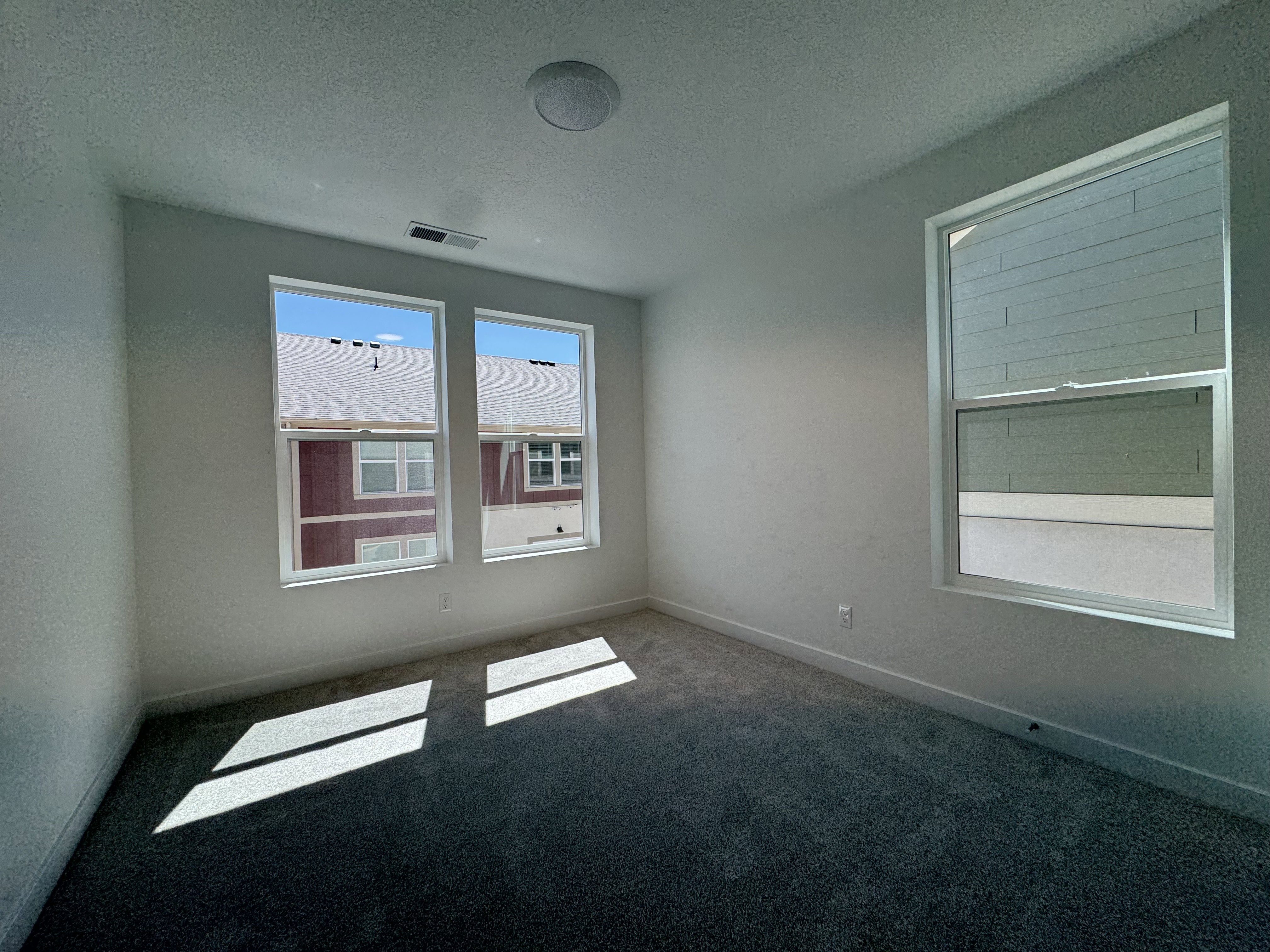 Interior room featuring a neutral color palette, dark gray carpeting, and multiple windows providing natural illumination