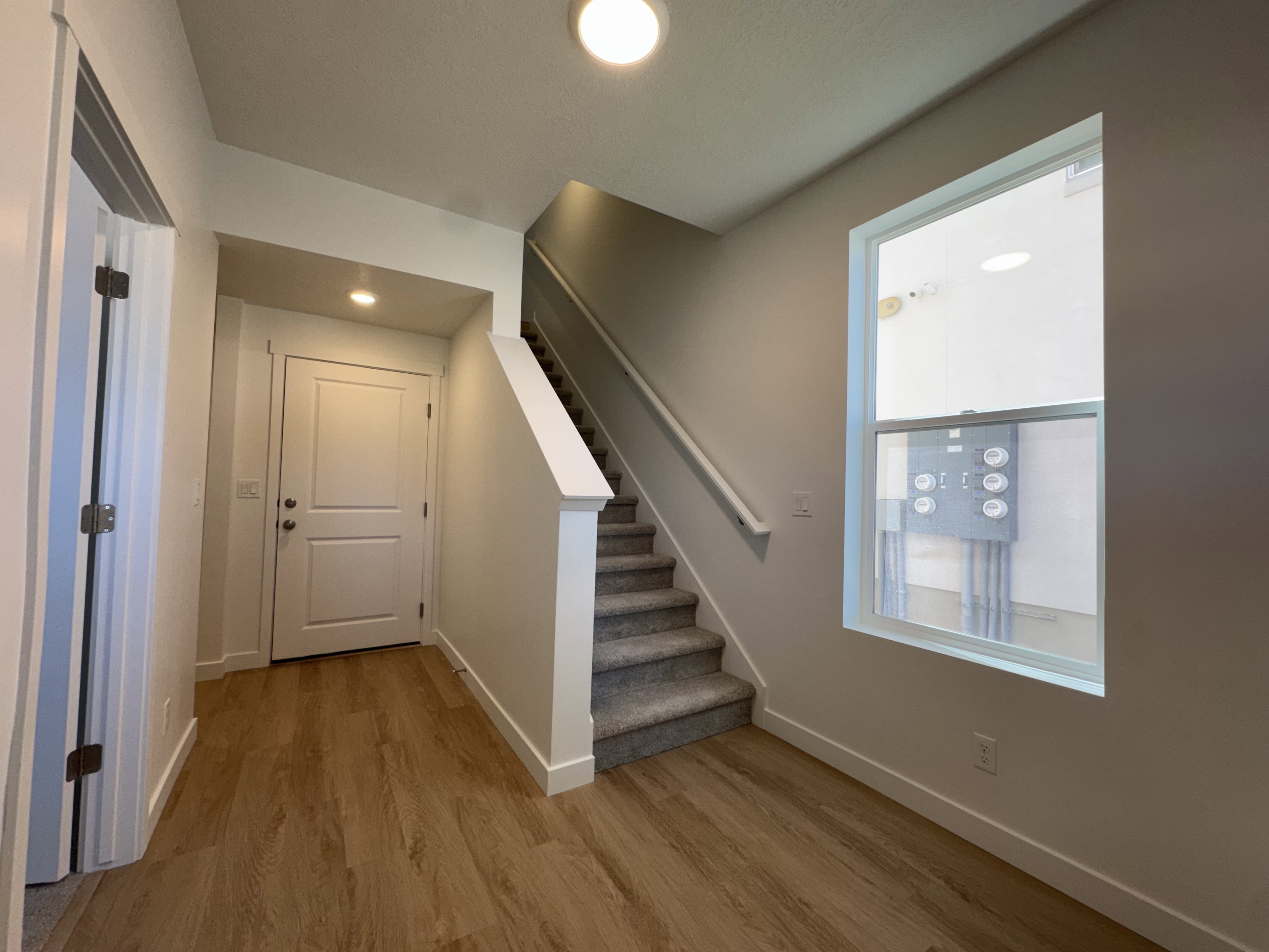 Entryway featuring wood-finish flooring, a white two-panel door, a carpeted staircase with white railing, and a window providing natural illumination